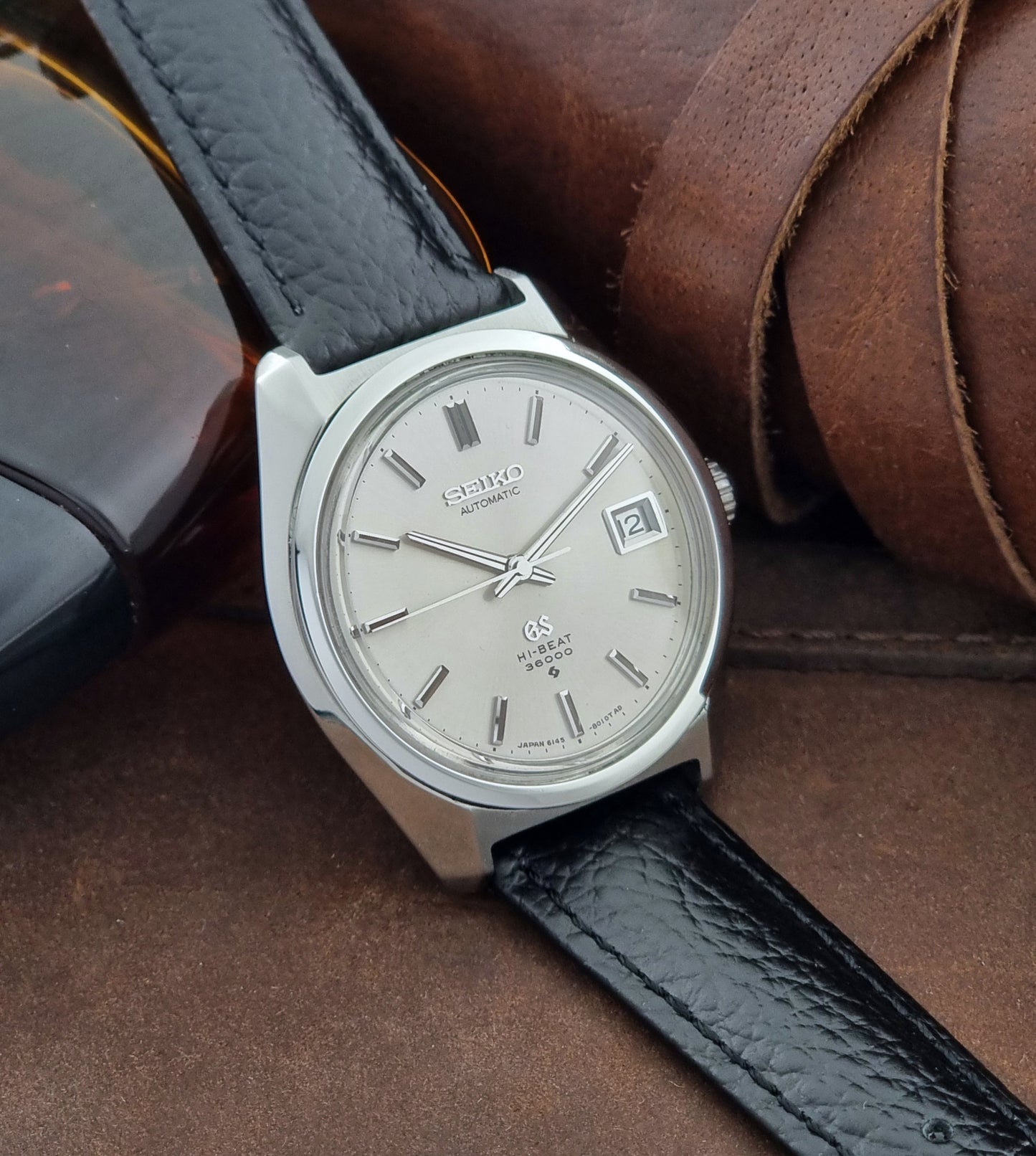 Grand Seiko Wristwatch 6145-8000 with black leather strap on a brown surface side view