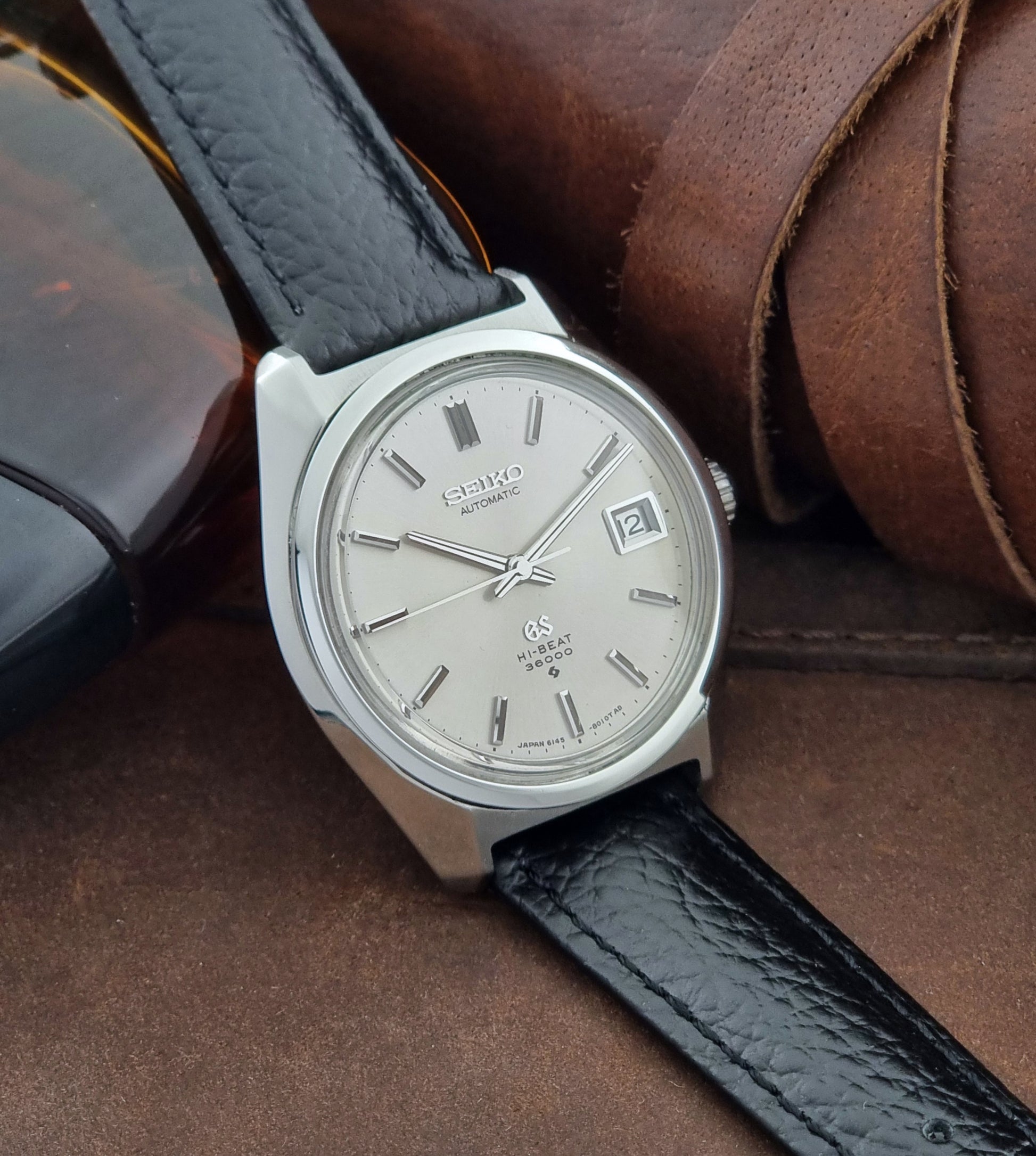 Grand Seiko Wristwatch 6145-8000 with black leather strap on a brown surface side view