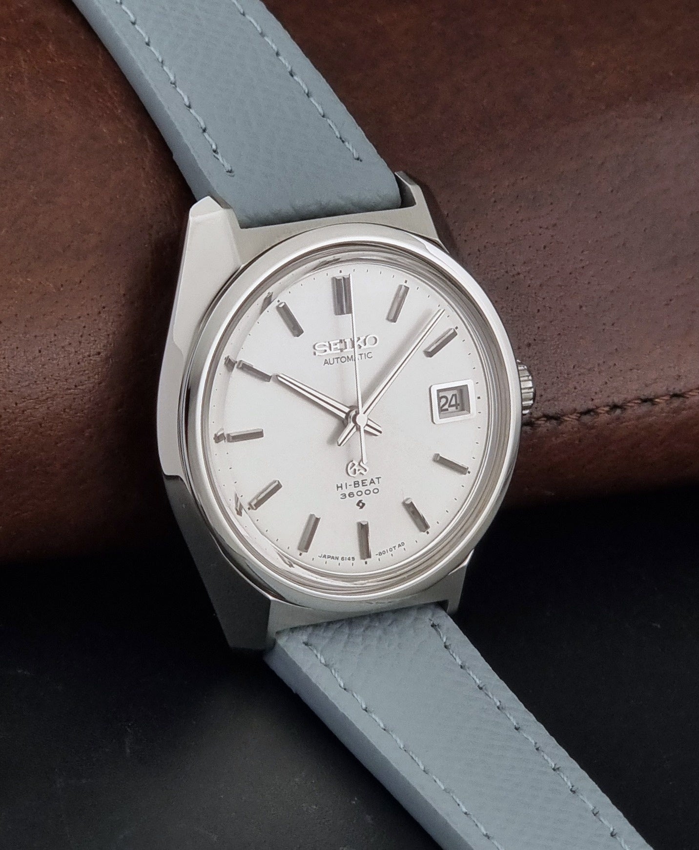 Vintage Grand Seiko 6145-8000 on a grey leather strap on a dark background side view