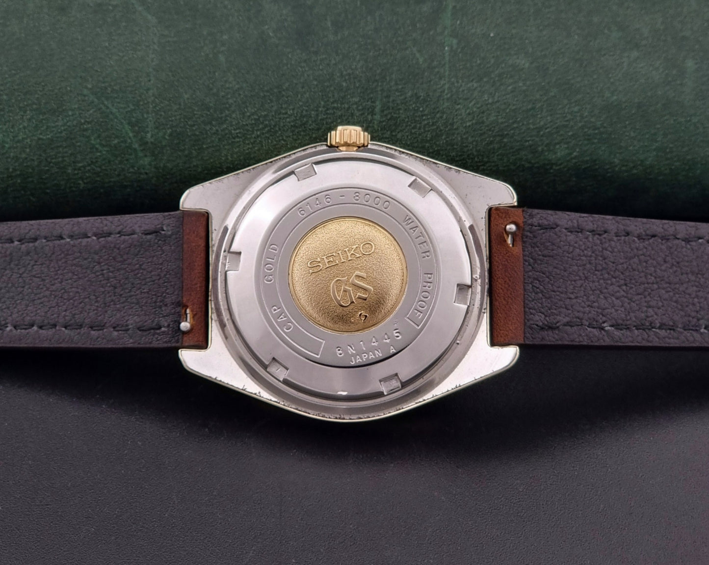 Vintage  Grand Seiko watch 6146-8000 watch with gold case and brown leather strap on a dark background case back view