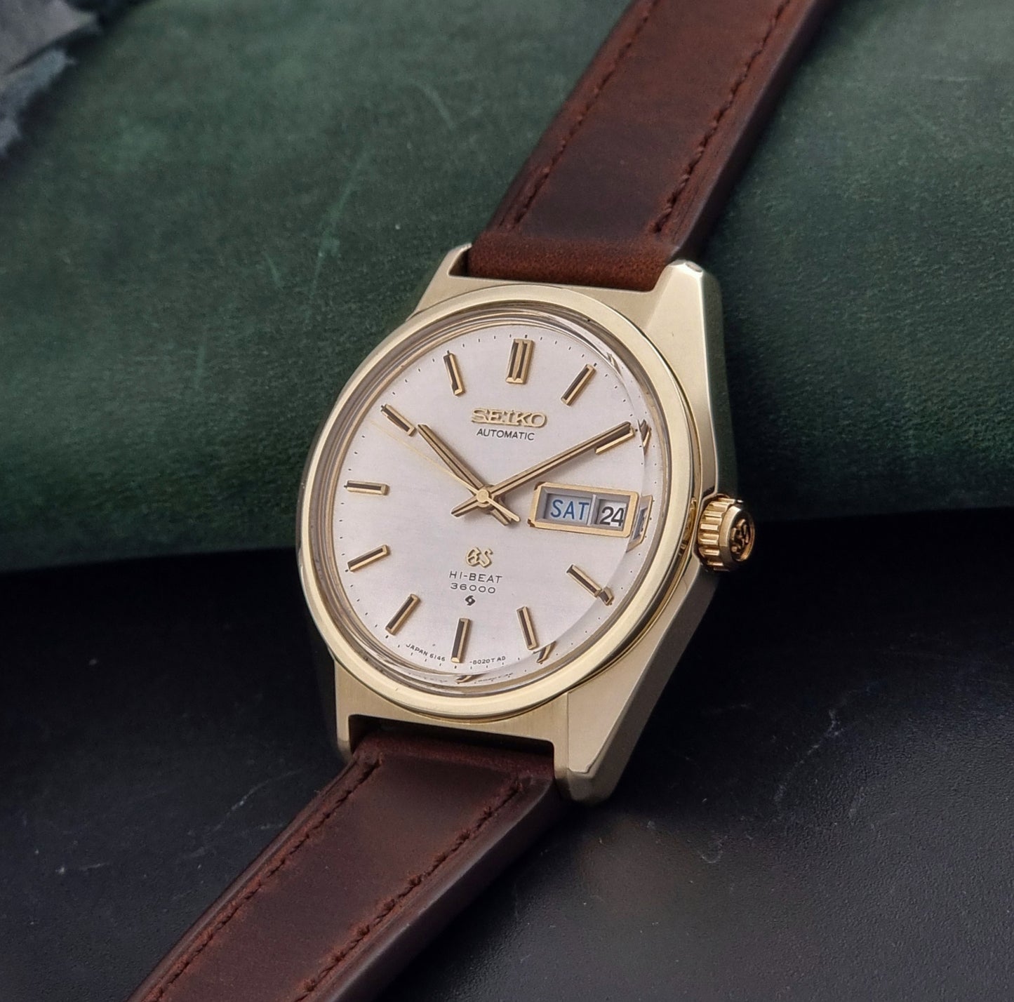 Vintage  Grand Seiko watch 6146-8000 watch with gold case and brown leather strap on a dark background crown view