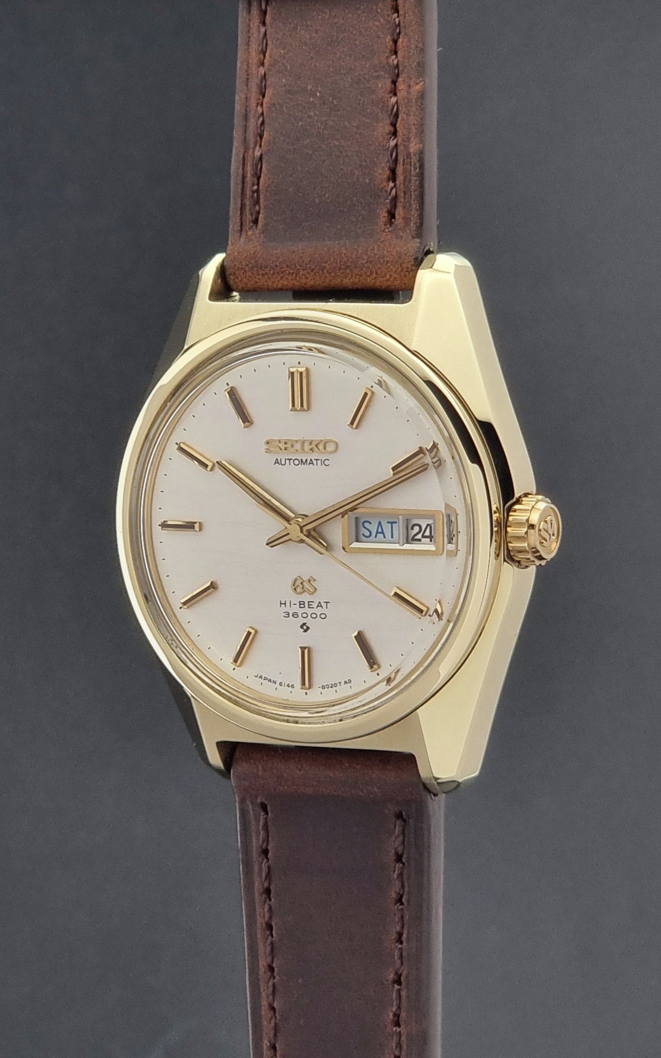 Vintage  Grand Seiko watch 6146-8000 watch with gold case and brown leather strap on a dark background crown profile view