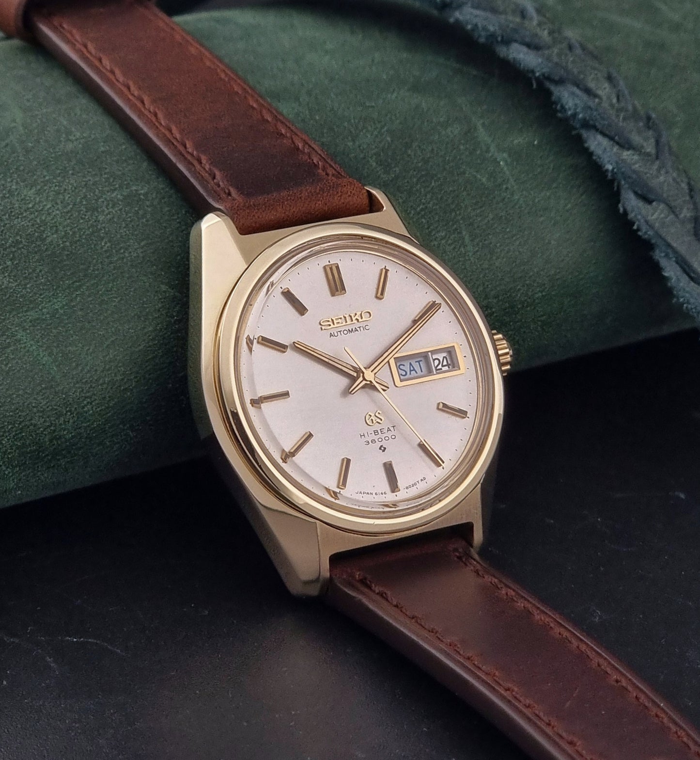 Vintage  Grand Seiko watch 6146-8000 watch with gold case and brown leather strap on a dark background side view