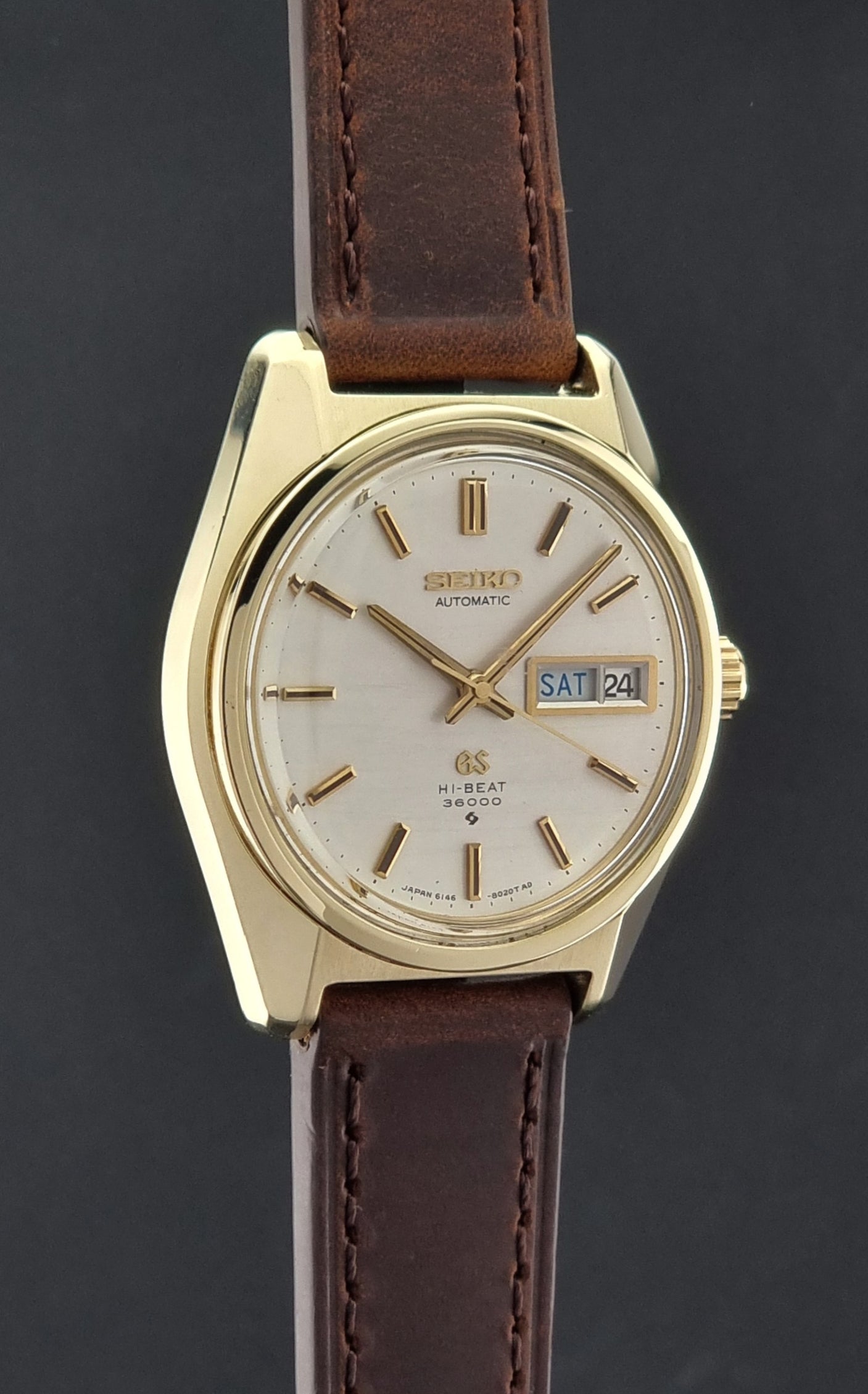 Vintage  Grand Seiko watch 6146-8000 watch with gold case and brown leather strap on a dark background side profile view