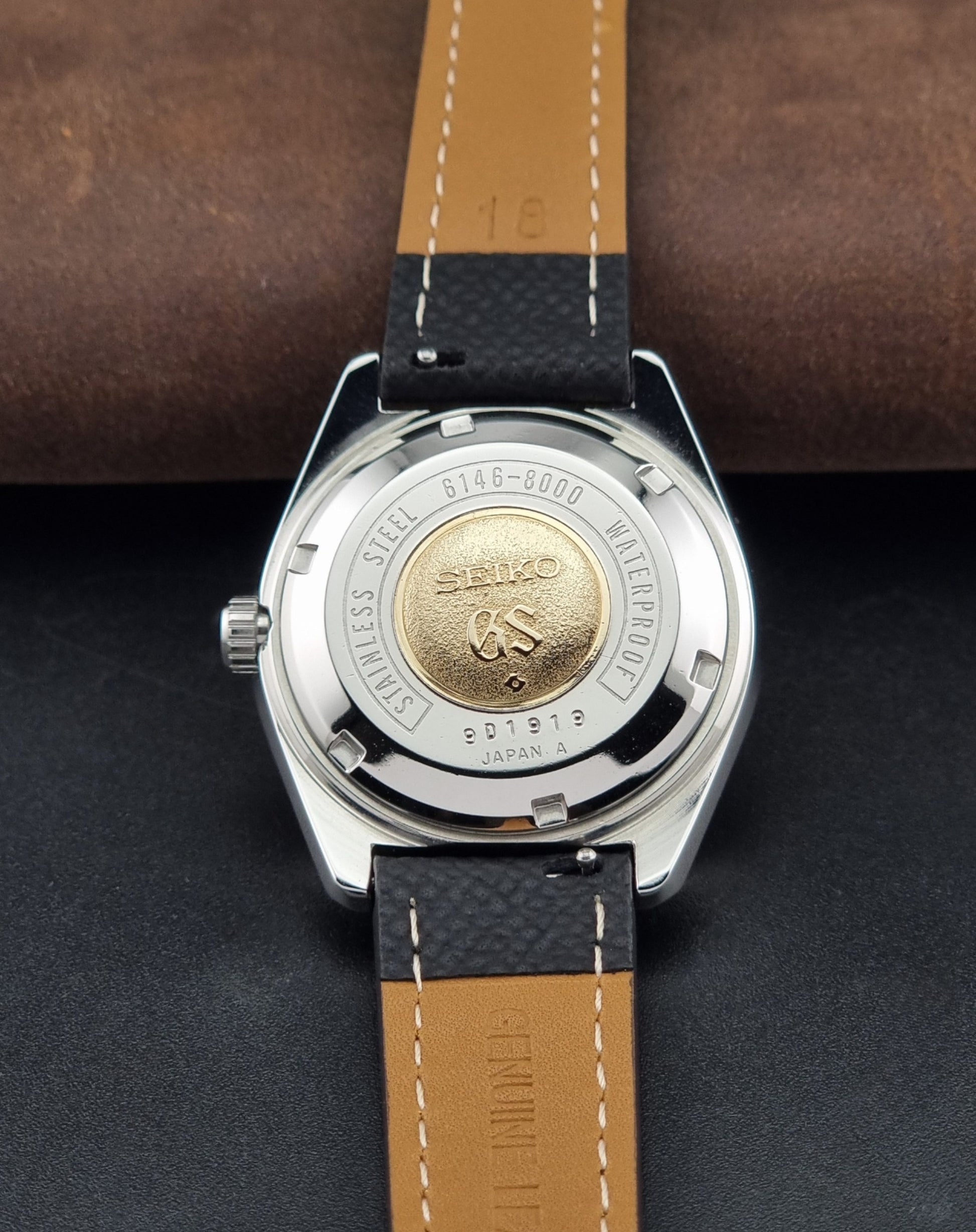Vintage Grand Seiko 6146-8000 Wristwatch with a black leather strap on a dark background case back view