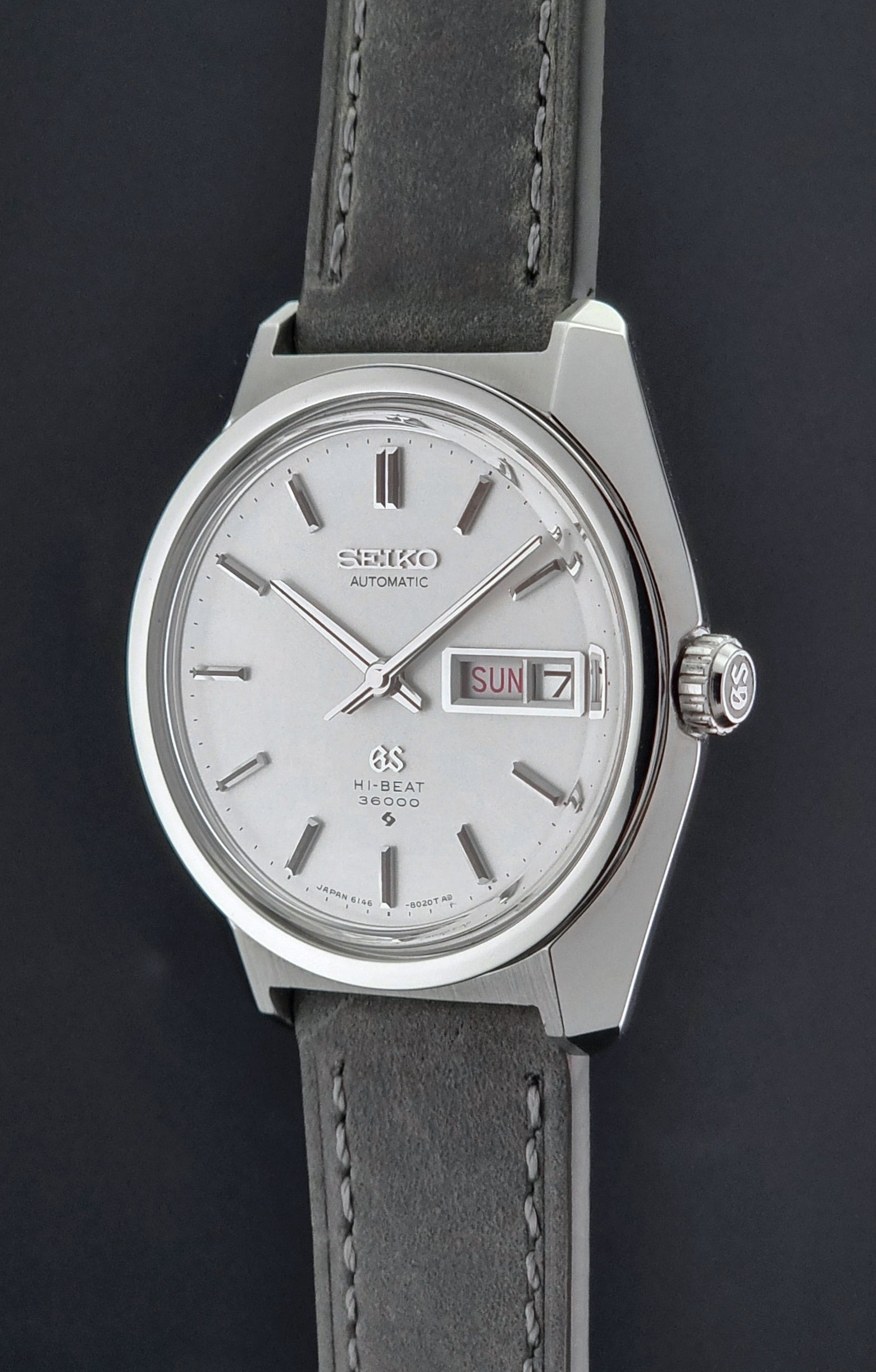 Vintage Grand Seiko Wristwatch 6146-8000 with gray strap and silver case on a dark grey background crown profile view