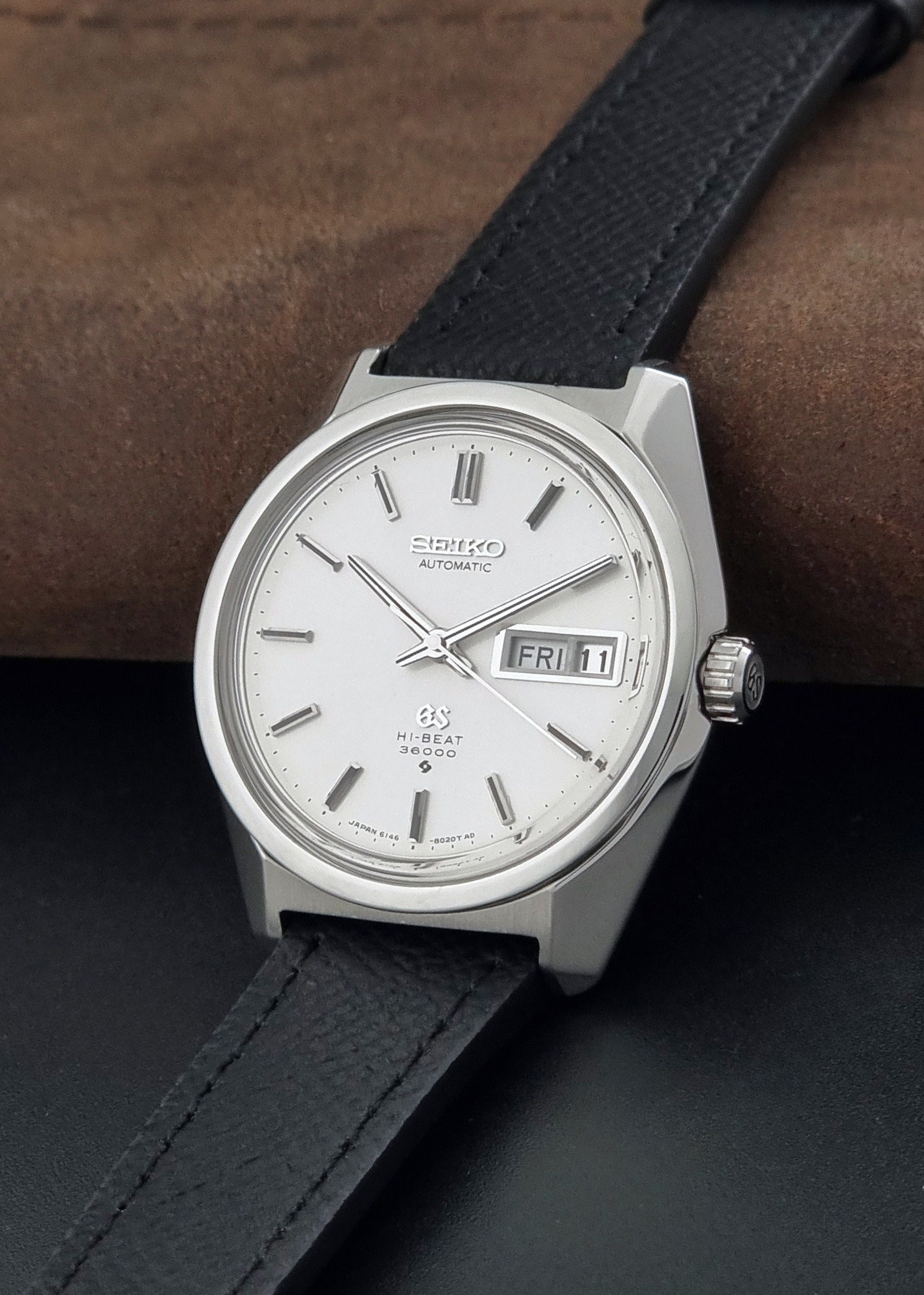 Vintage Grand Seiko 6146-8000 Wristwatch with a black leather strap on a dark background crown view