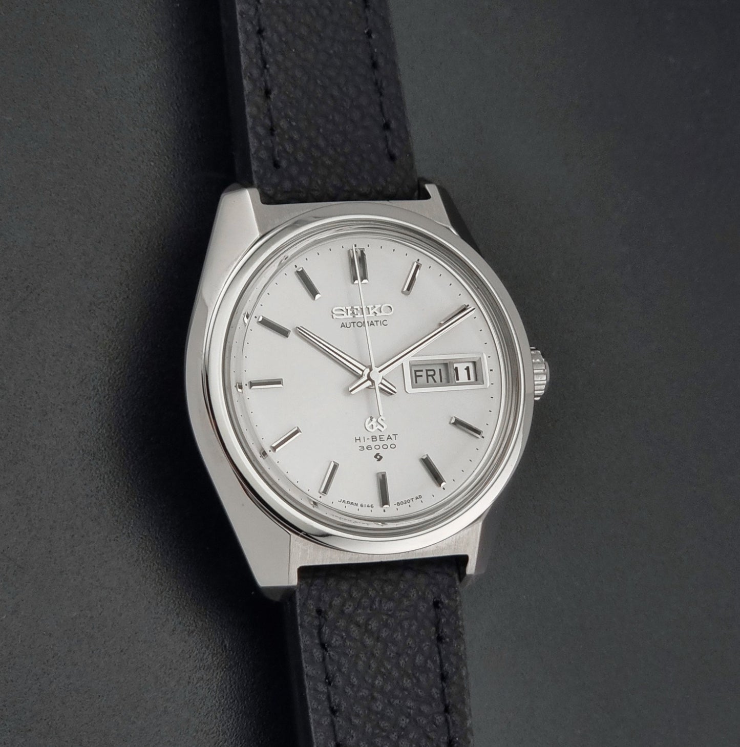 Vintage Grand Seiko 6146-8000 Wristwatch with a black leather strap on a dark background front view