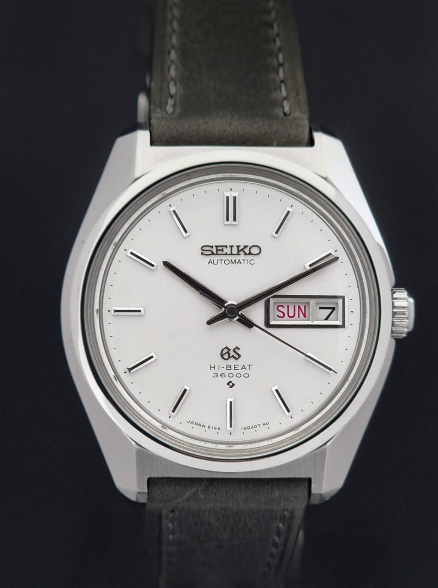 Vintage Grand Seiko Wristwatch 6146-8000 with gray strap and silver case on a dark grey background close front view