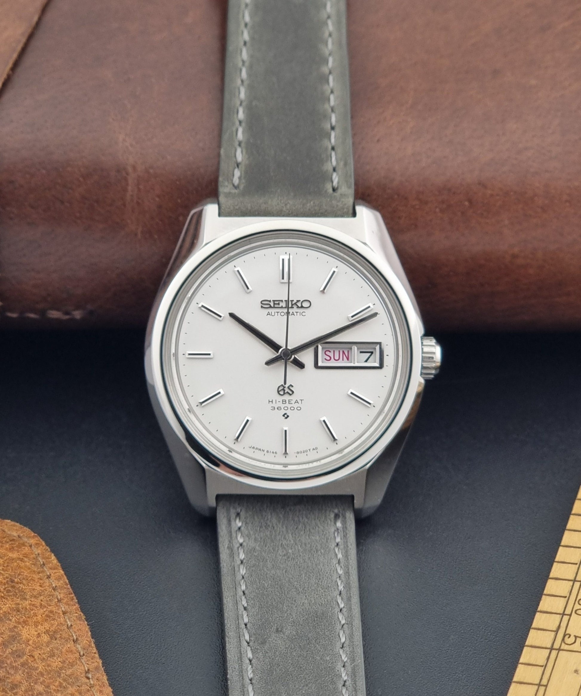 Vintage Grand Seiko Wristwatch 6146-8000 with gray strap and silver case on a dark grey background front view