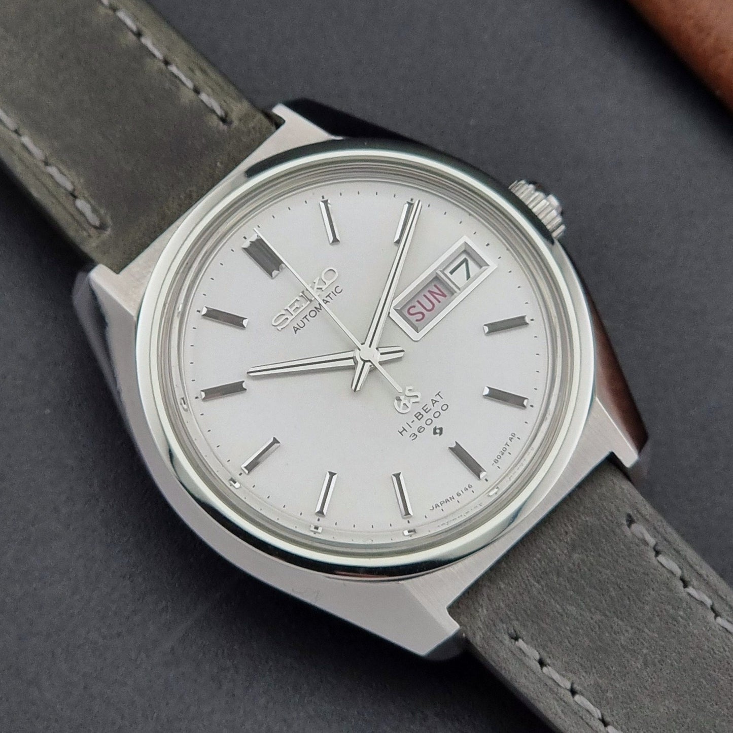 Vintage Grand Seiko Wristwatch 6146-8000 with gray strap and silver case on a dark grey background close dial view