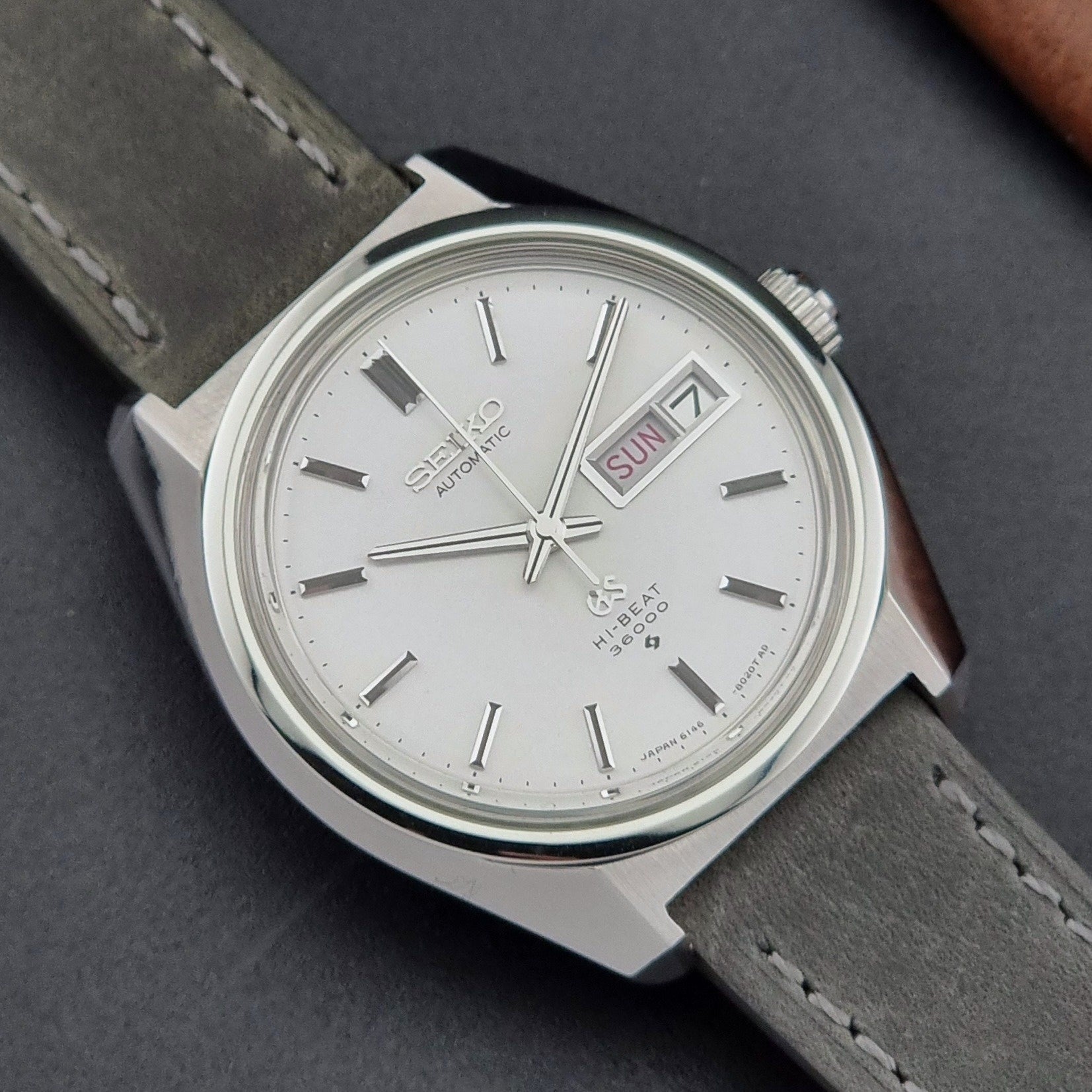 Vintage Grand Seiko Wristwatch 6146-8000 with gray strap and silver case on a dark grey background close dial view