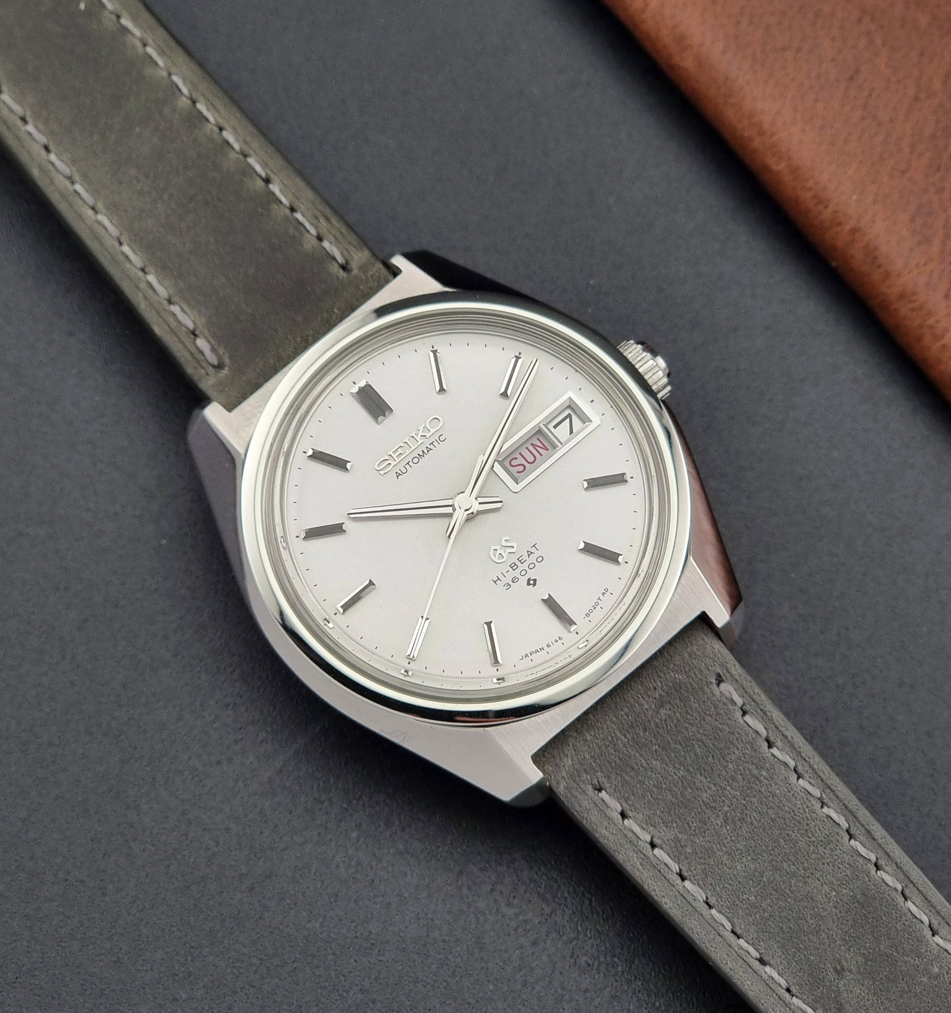 Vintage Grand Seiko Wristwatch 6146-8000 with gray strap and silver case on a dark grey background front