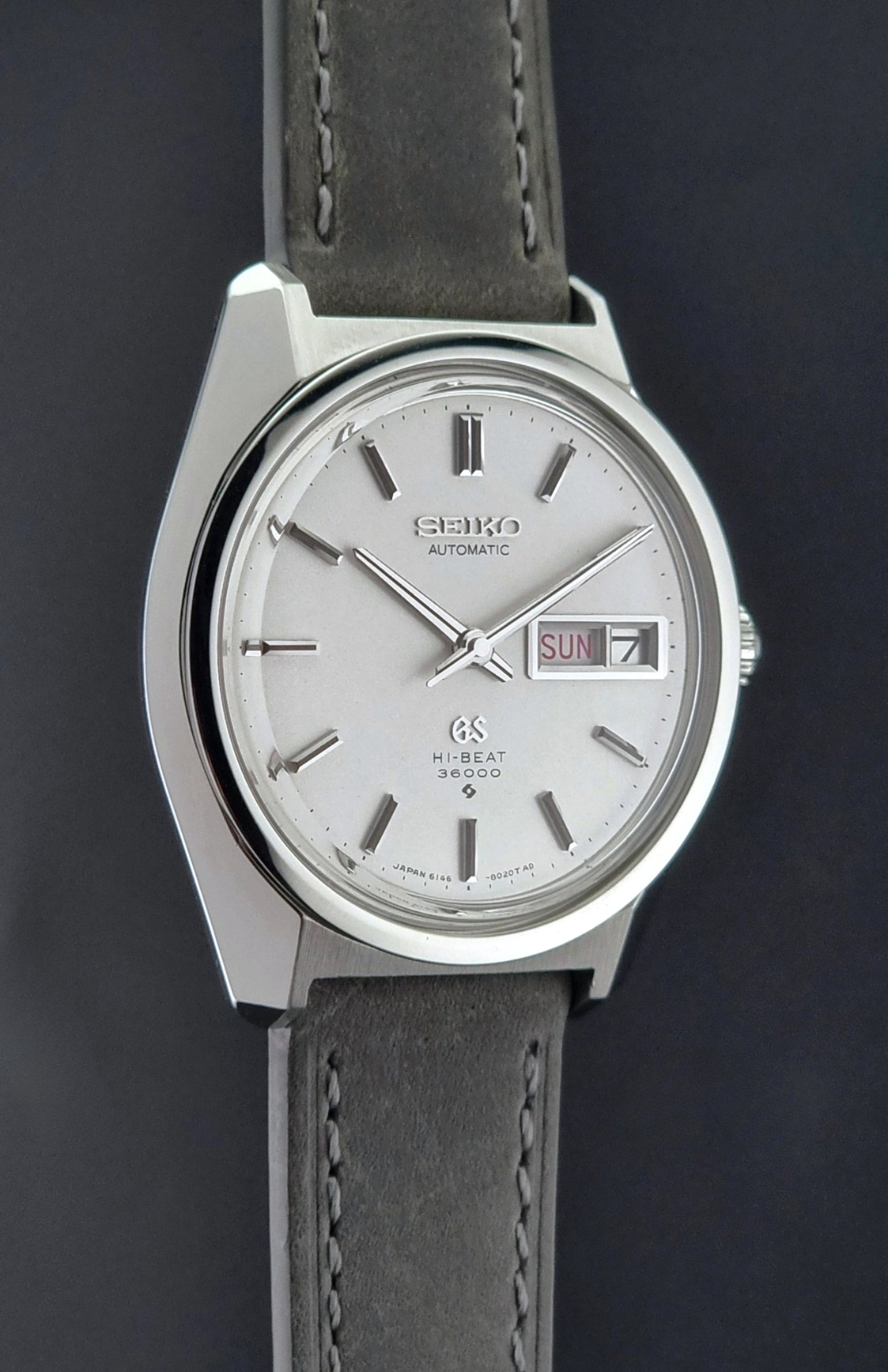 Vintage Grand Seiko Wristwatch 6146-8000 with gray strap and silver case on a dark grey background side profile view