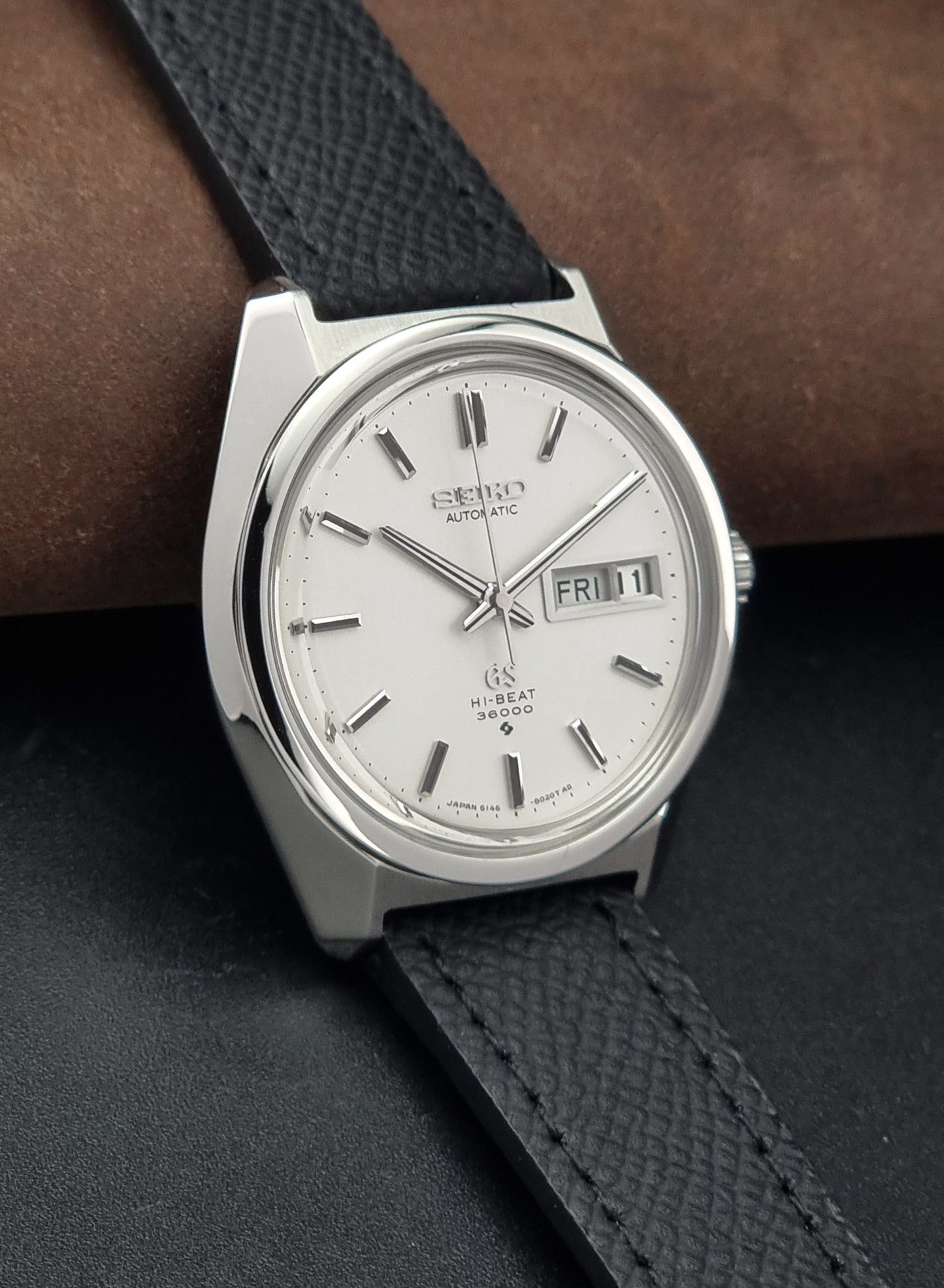 Vintage Grand Seiko 6146-8000 Wristwatch with a black leather strap on a dark background side view
