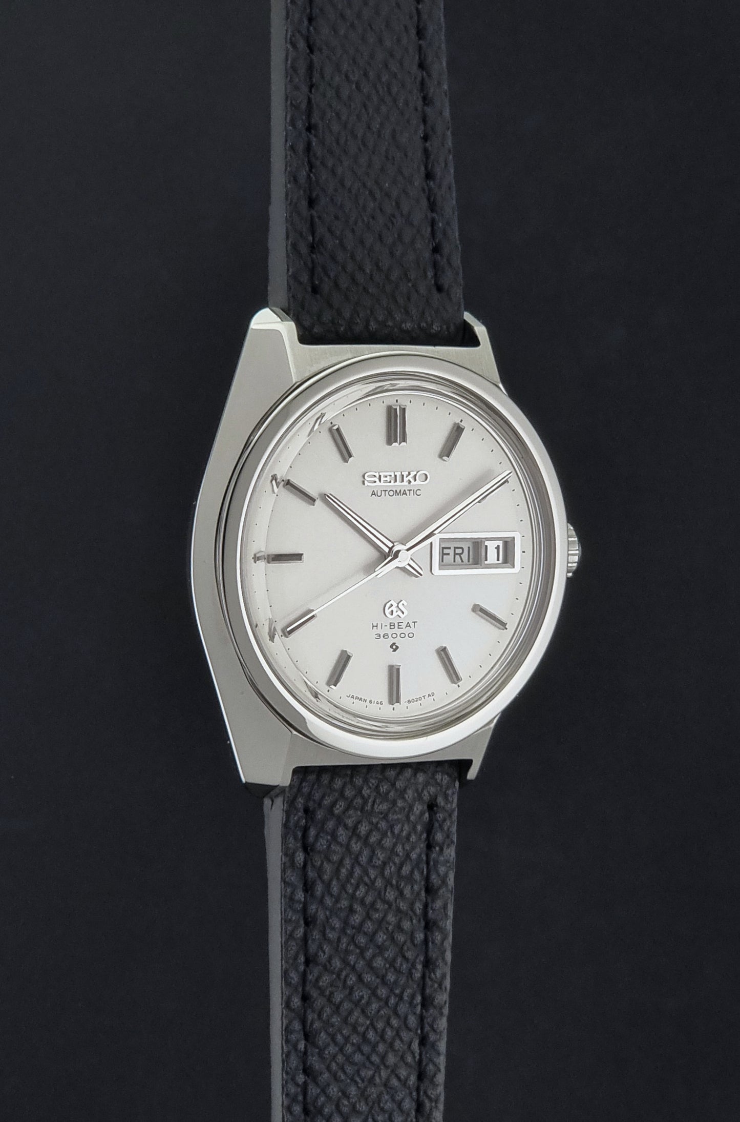 Vintage Grand Seiko 6146-8000 Wristwatch with a black leather strap on a dark background side profile view