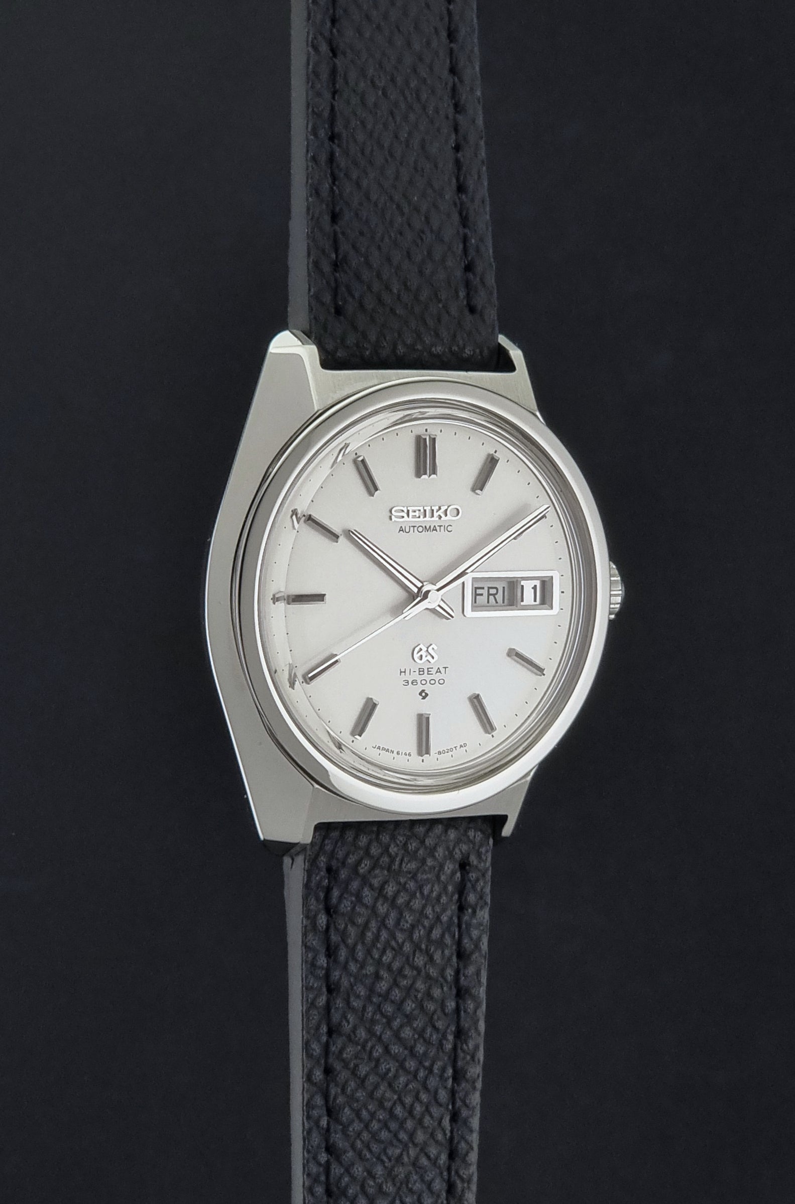 Vintage Grand Seiko 6146-8000 Wristwatch with a black leather strap on a dark background side profile view