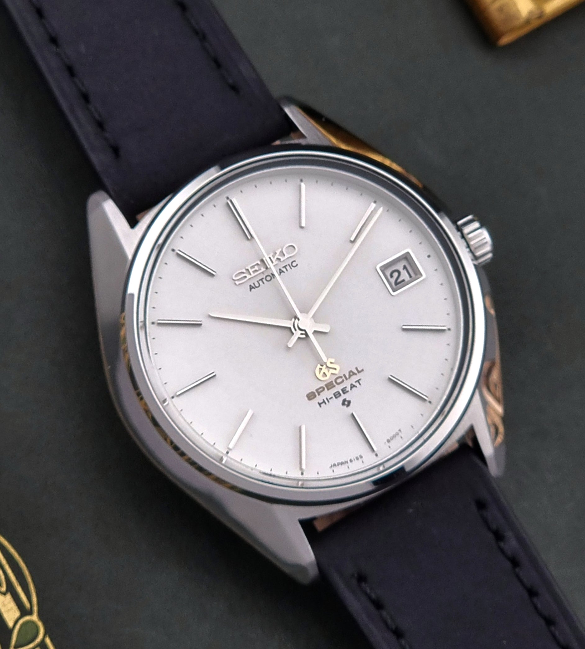 Vintage Grand Seiko Wristwatch with a white face and black leather strap on a dark background