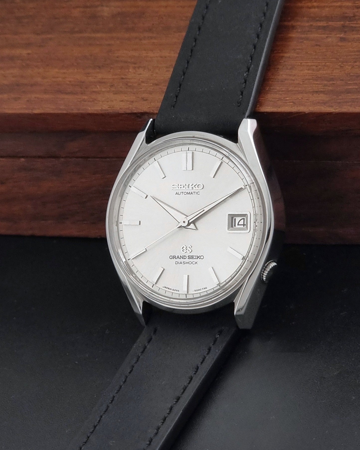 Vintage Grand Seiko 6245-9001 Wristwatch with a black leather strap on a dark background crown view
