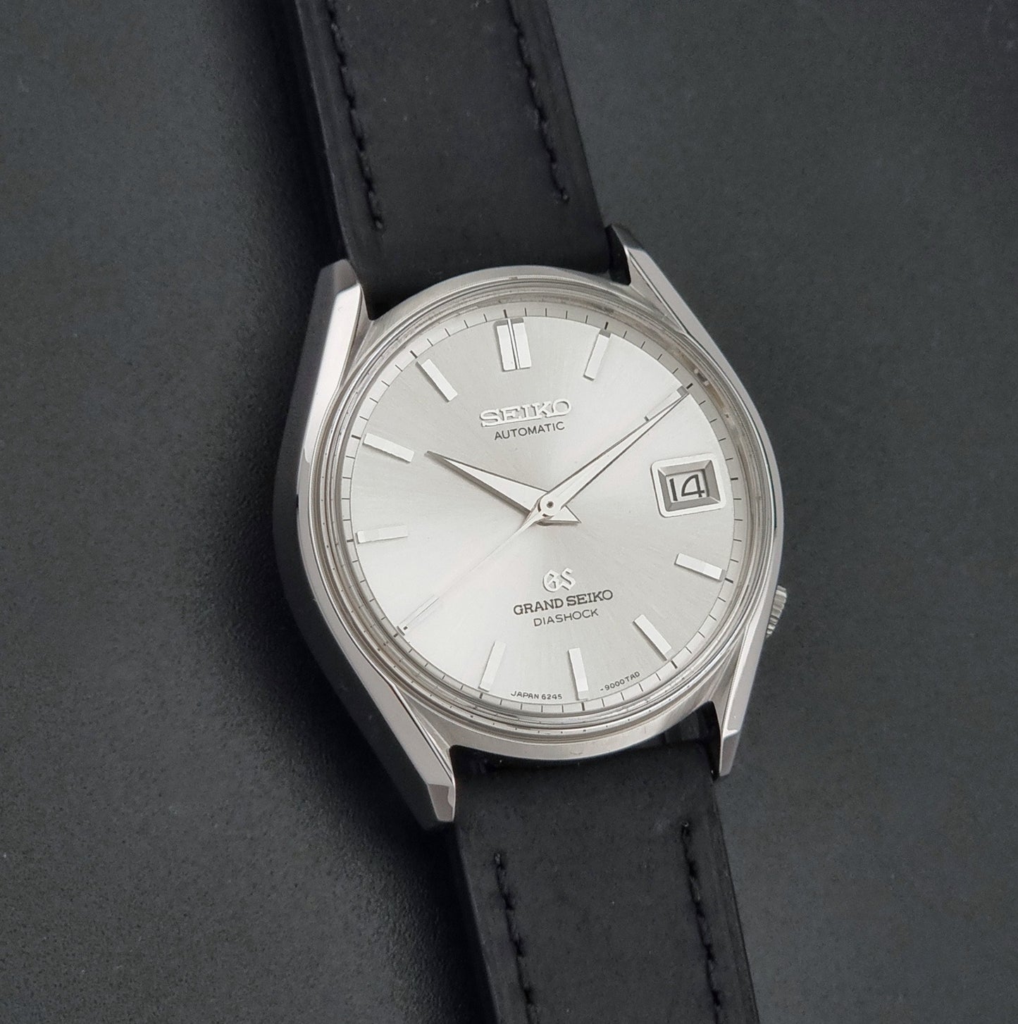Vintage Grand Seiko 6245-9001 Wristwatch with a black leather strap on a dark background front view
