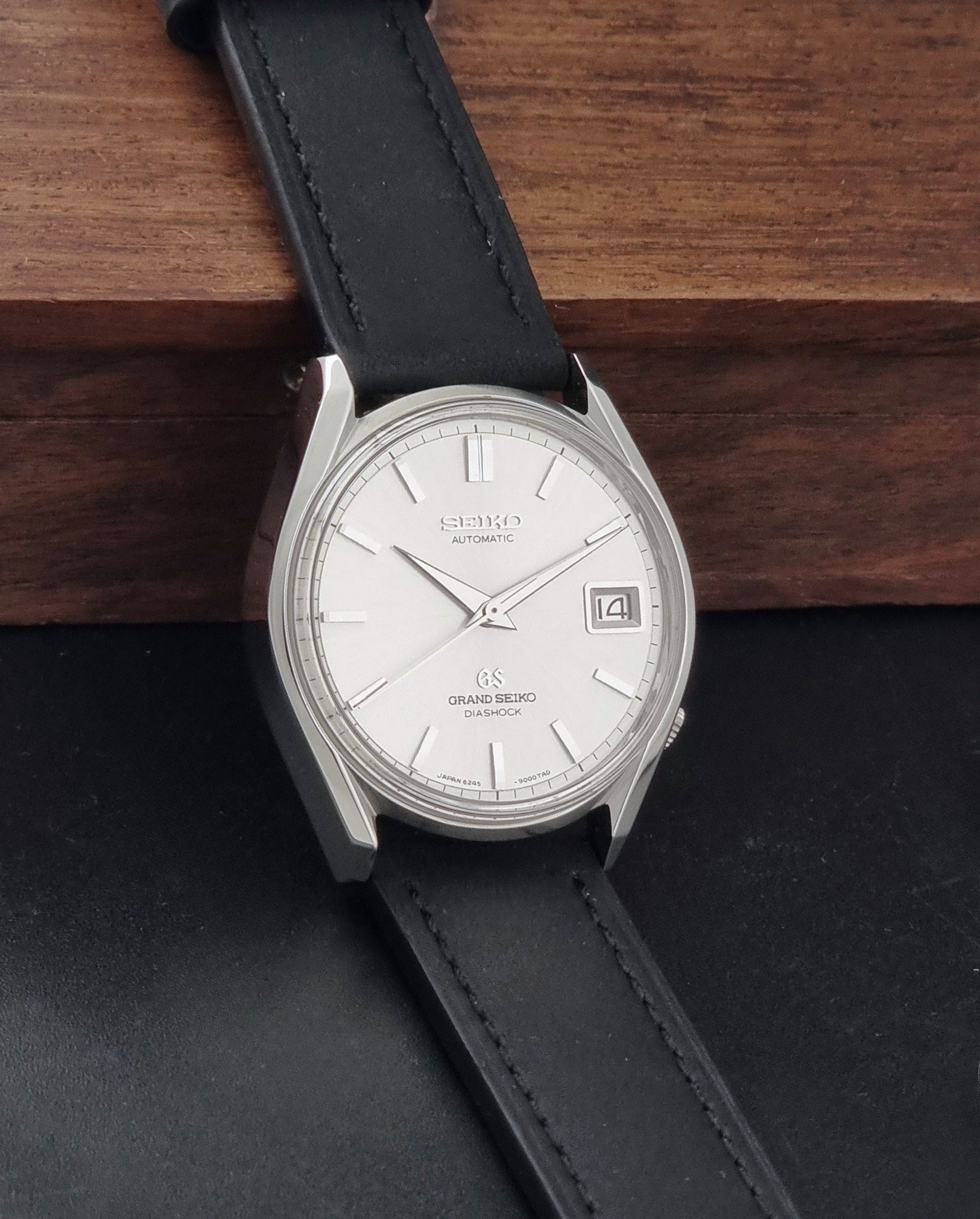 Vintage Grand Seiko 6245-9001 Wristwatch with a black leather strap on a dark background side view