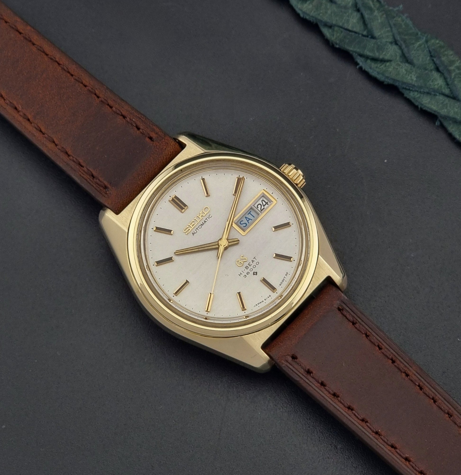 Vintage  Grand Seiko watch 6146-8000 watch with gold case and brown leather strap on a dark background dial