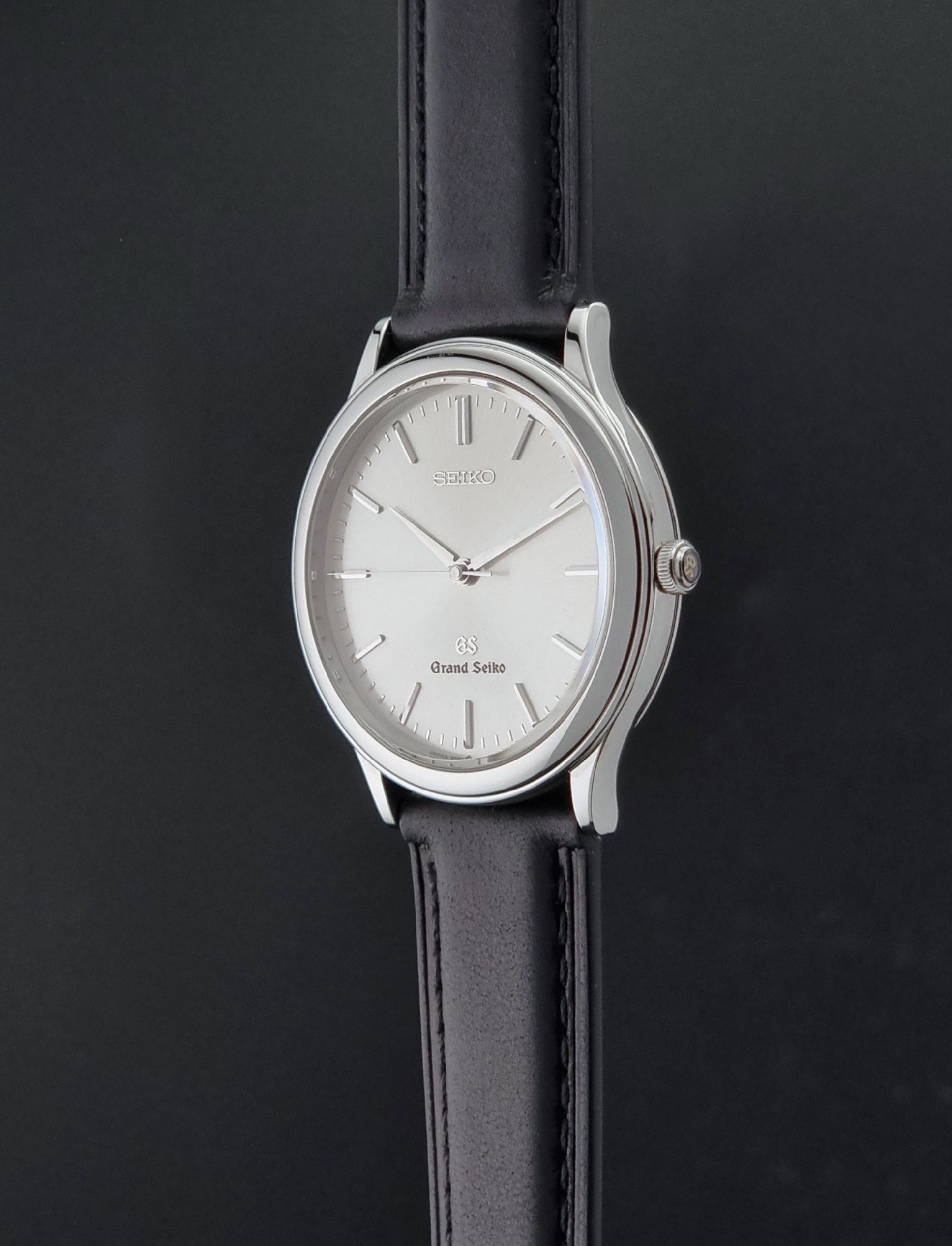 Vintage Grand Seiko 9581-7000 Quartz with black strap and silver case on a brown background crown profile view