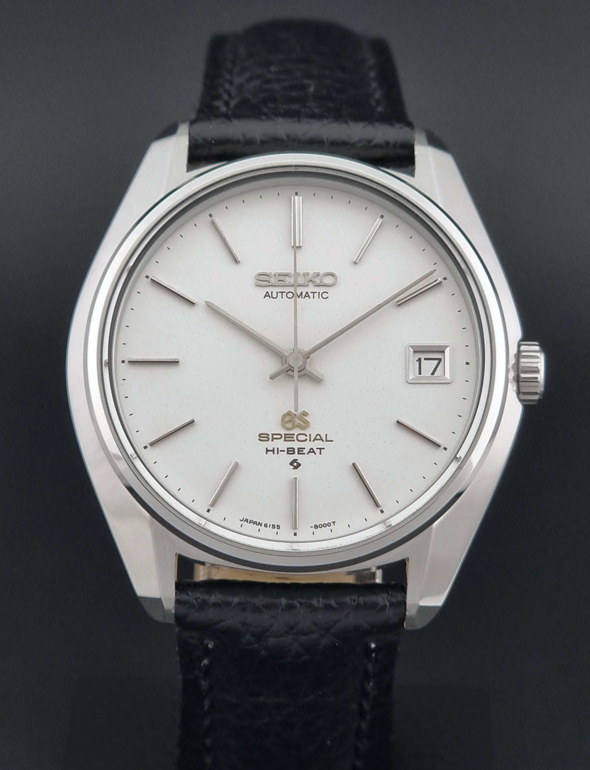 Vintage Grand Seiko Special 6155-8000 Silver wristwatch with black leather strap on a gray background dial view