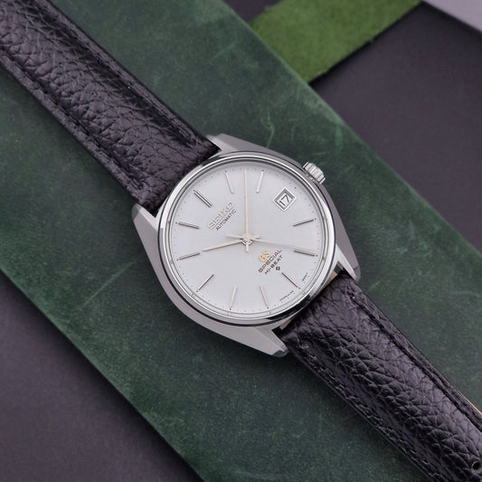Vintage Grand Seiko Special 6155-8000 Silver wristwatch with black leather strap on a green and gray background front