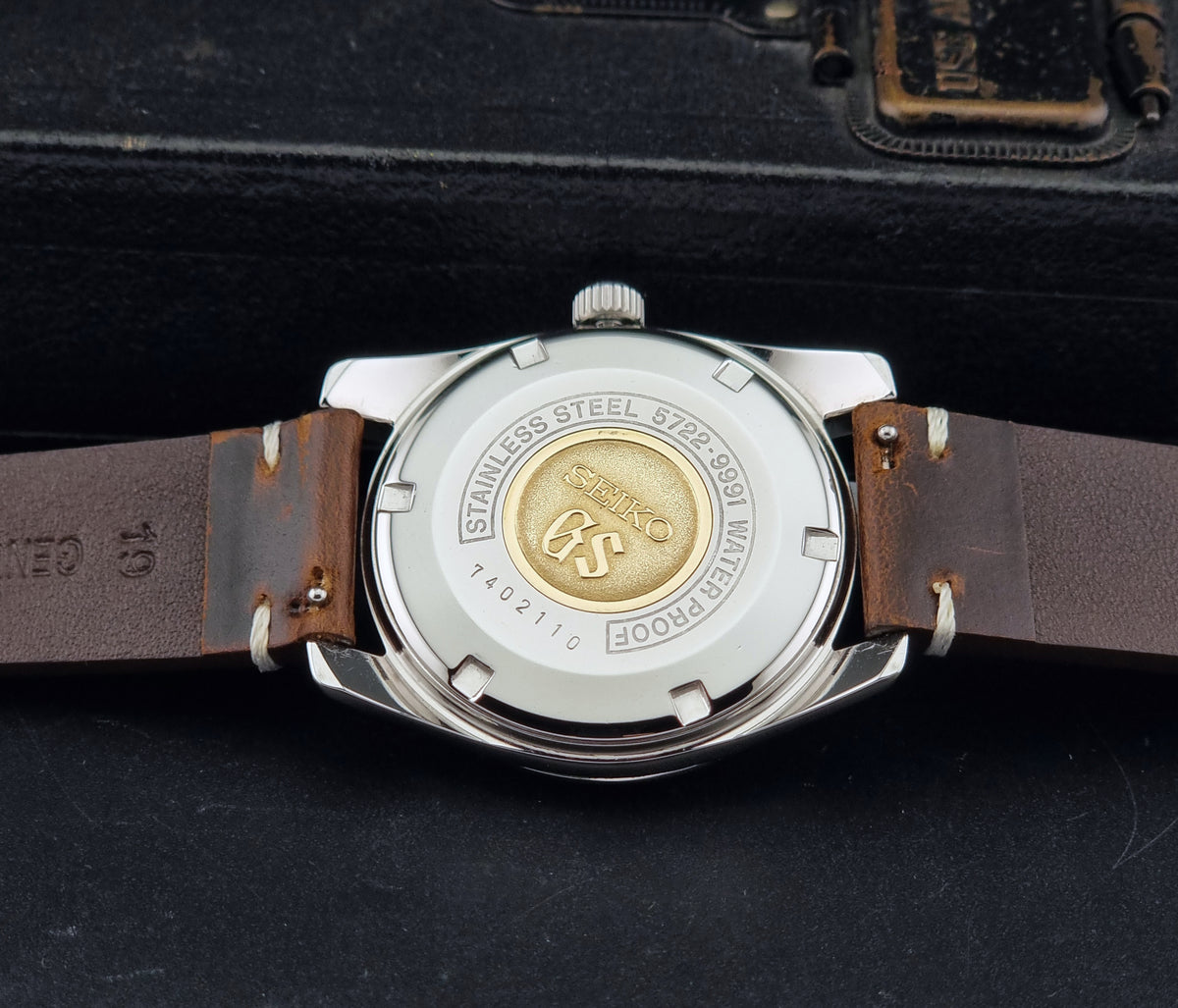 Vintage Grand Seiko 5722-9991 wristwatch with a silver dial, silver case, and a brown leather strap, shown on a dark gray background back view