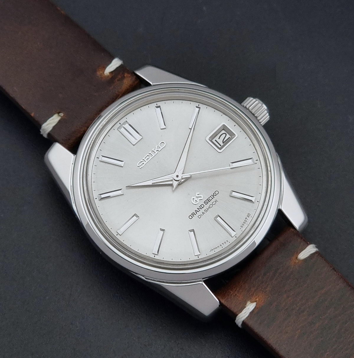 Vintage Grand Seiko 5722-9991 wristwatch with a silver dial, silver case, and a brown leather strap, shown on a dark gray background close up dial view