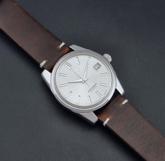 Vintage Grand Seiko 5722-9991 wristwatch with a silver dial, silver case, and a brown leather strap, shown on a dark gray background dial