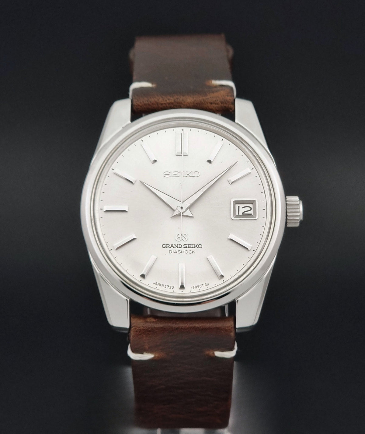 Vintage Grand Seiko 5722-9991 wristwatch with a silver dial, silver case, and a brown leather strap, shown on a dark gray background close dial view