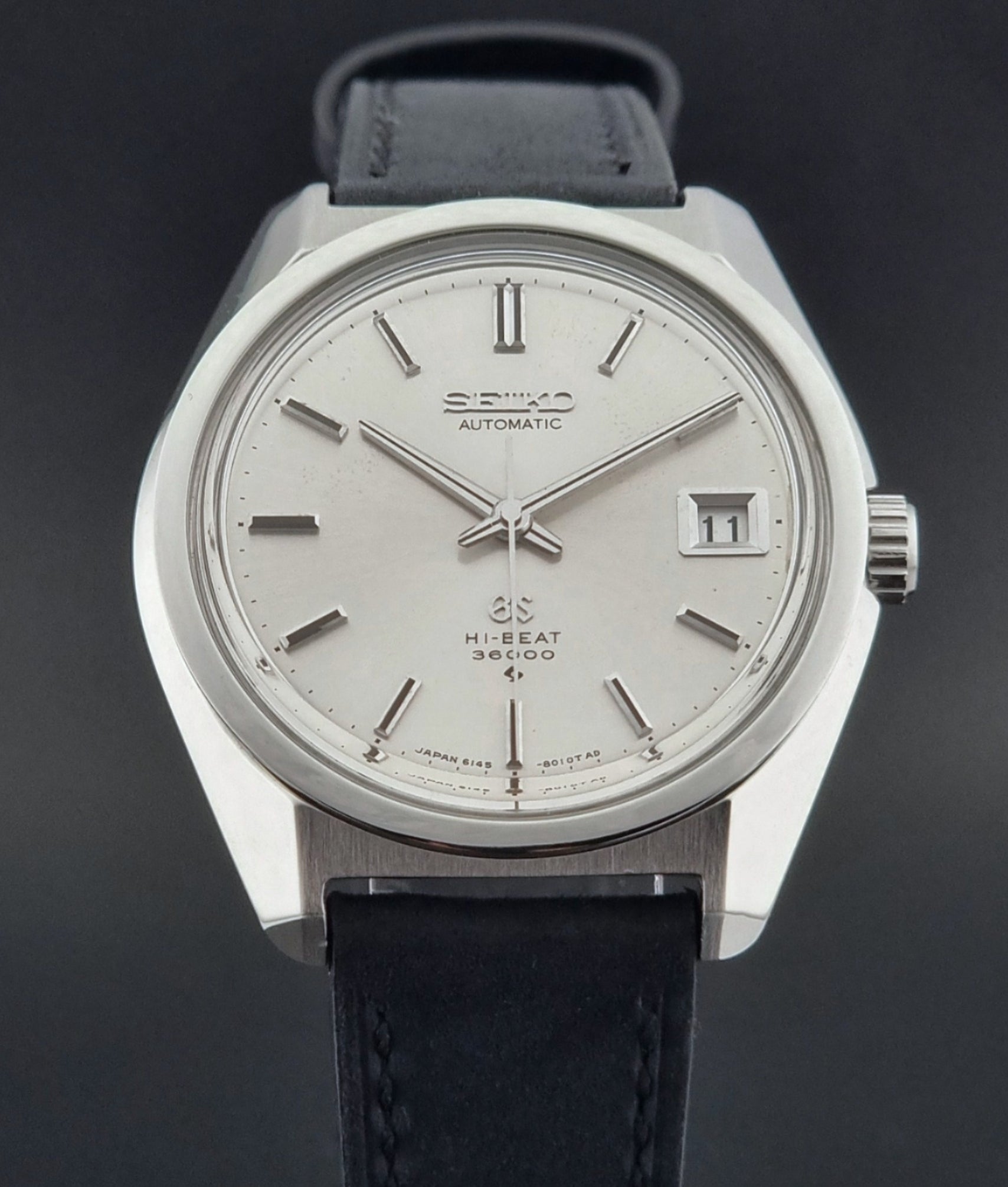 Vintage watch with black leather strap and silver case on a dark background