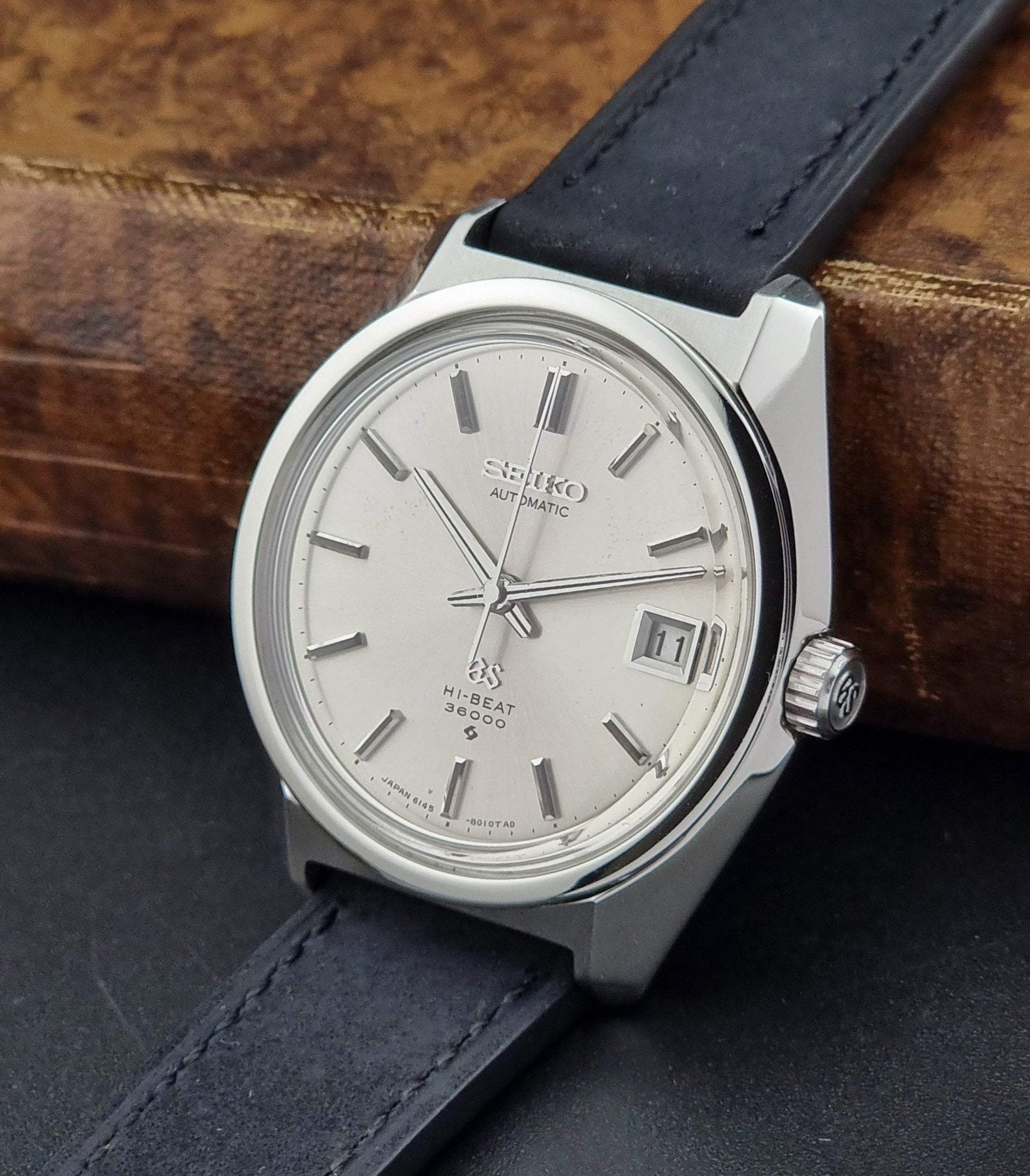 Seiko watch with silver dial and black leather strap on a wooden surface