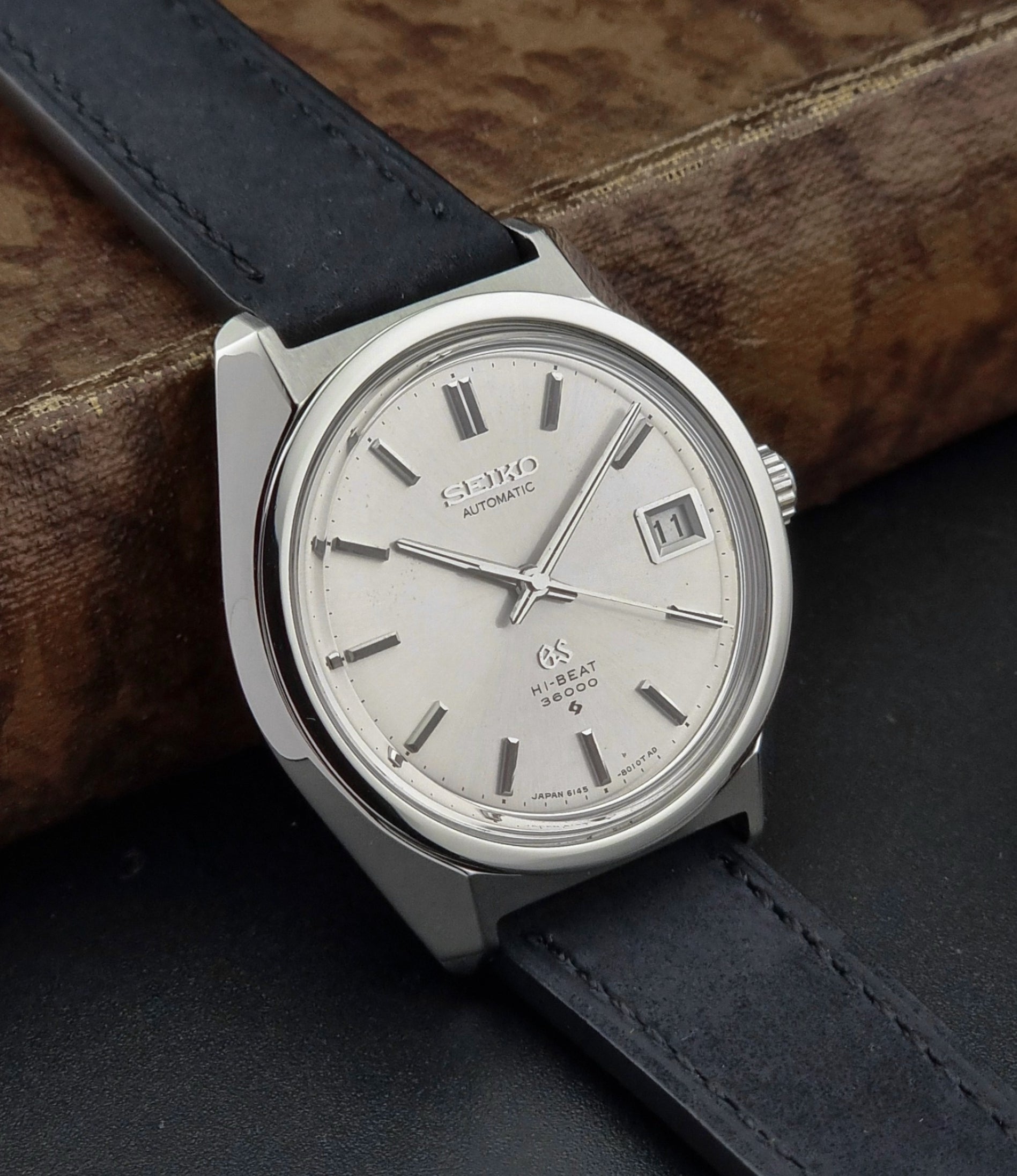Silver Seiko watch with black leather strap on a wooden surface