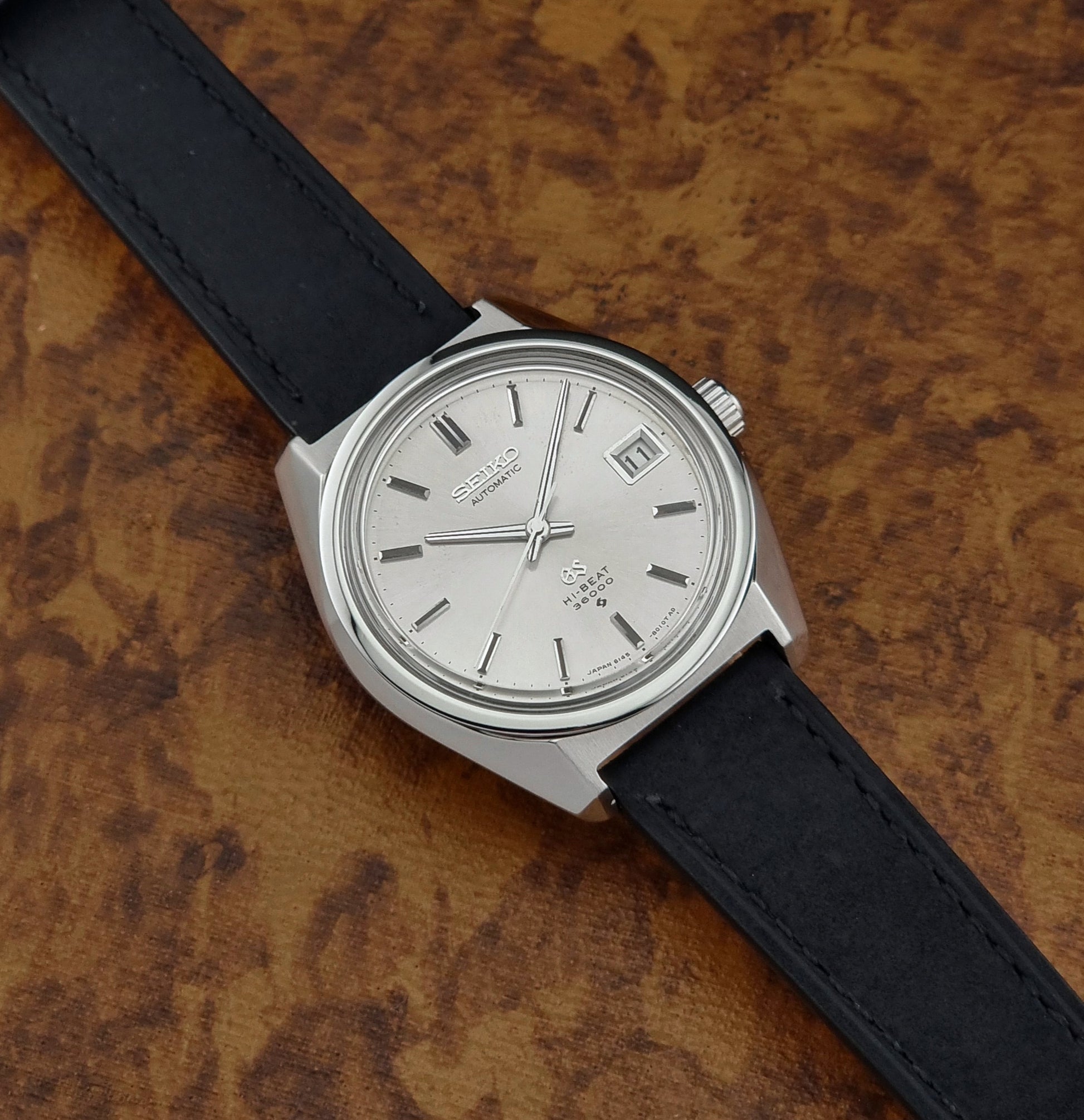 Wristwatch with black strap and silver case on a textured brown background