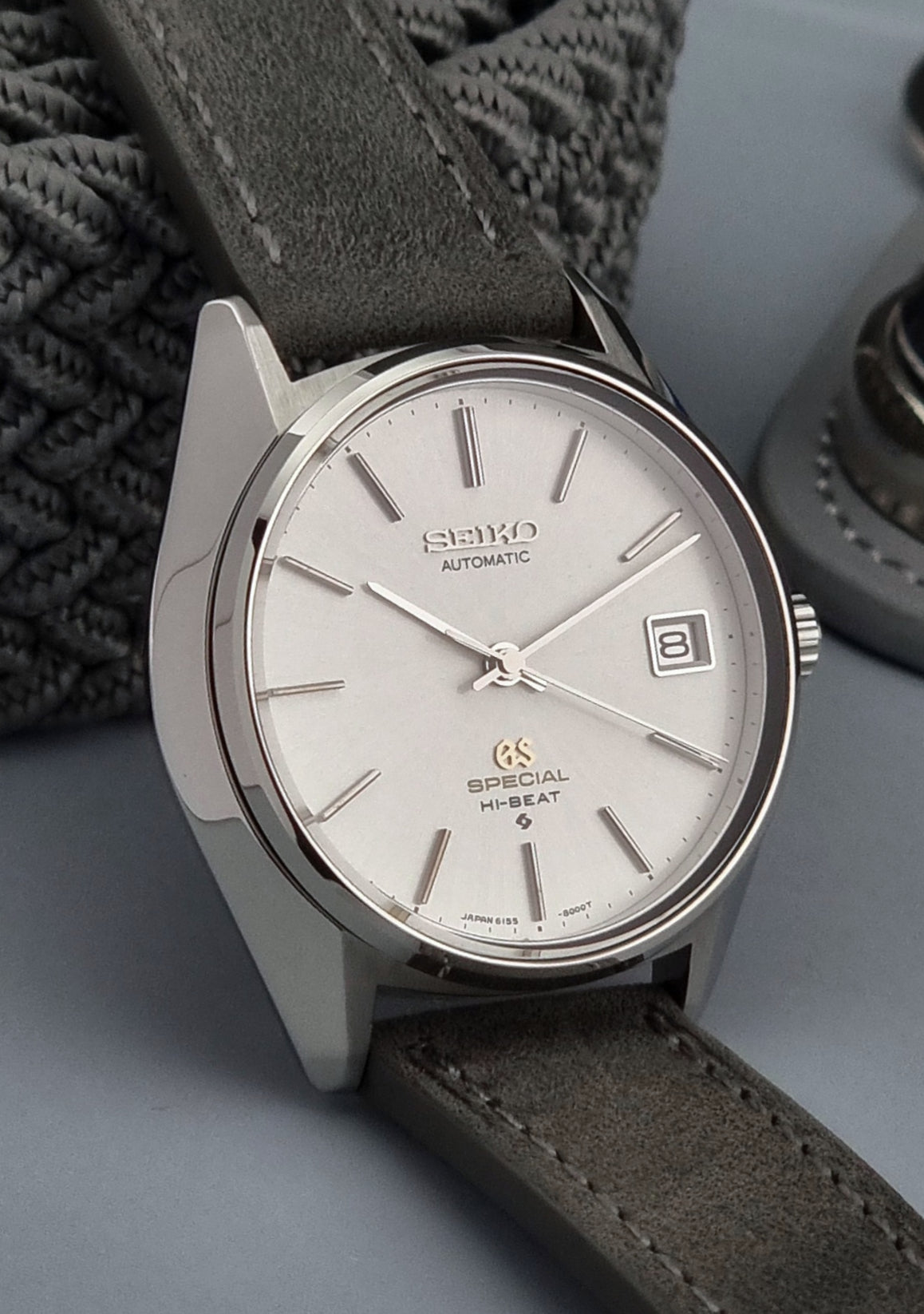 Grand Seiko wristwatch with a leather strap and silver case on a gray background