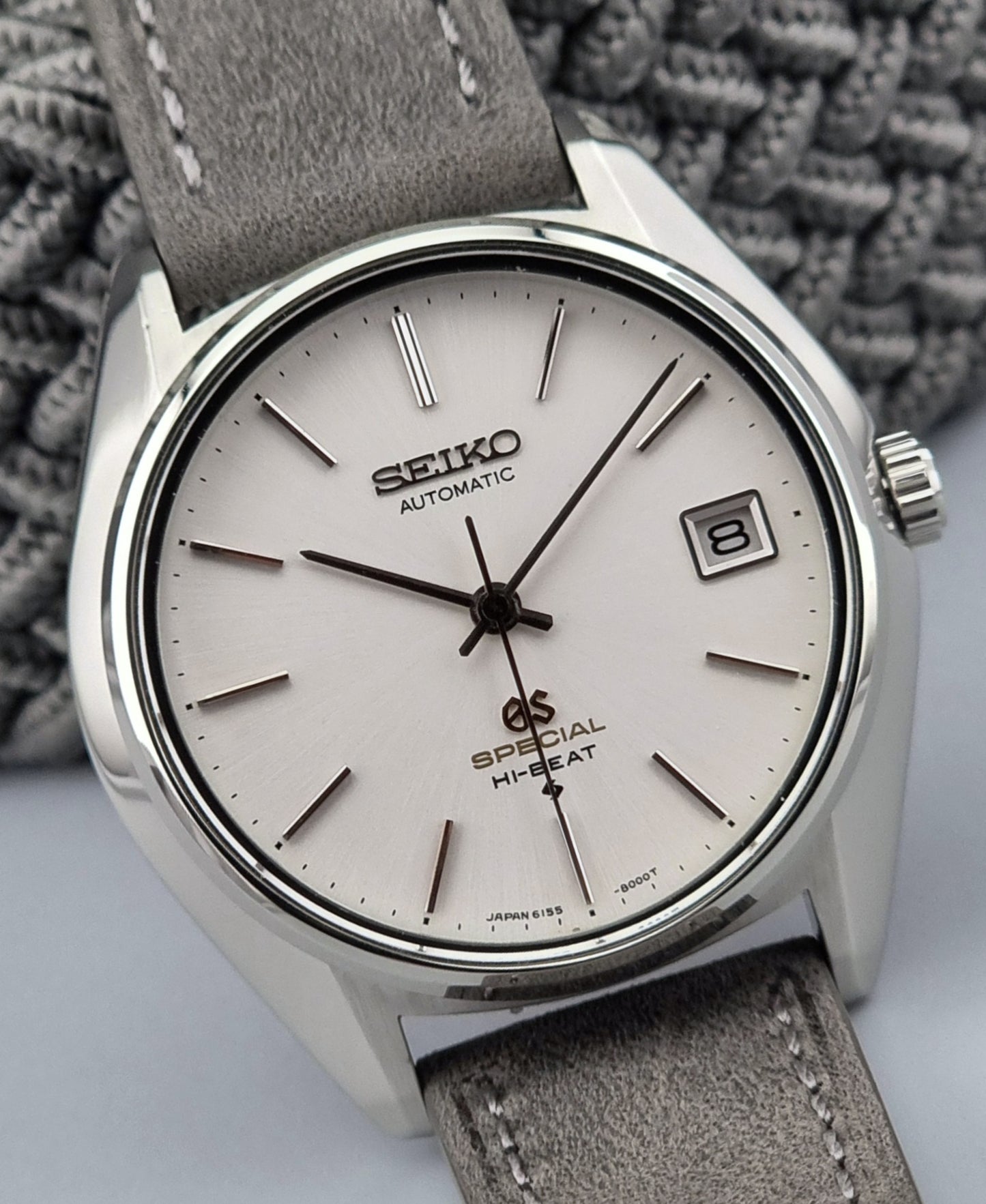 Grand Seiko wristwatch with a leather strap and silver case on a gray background