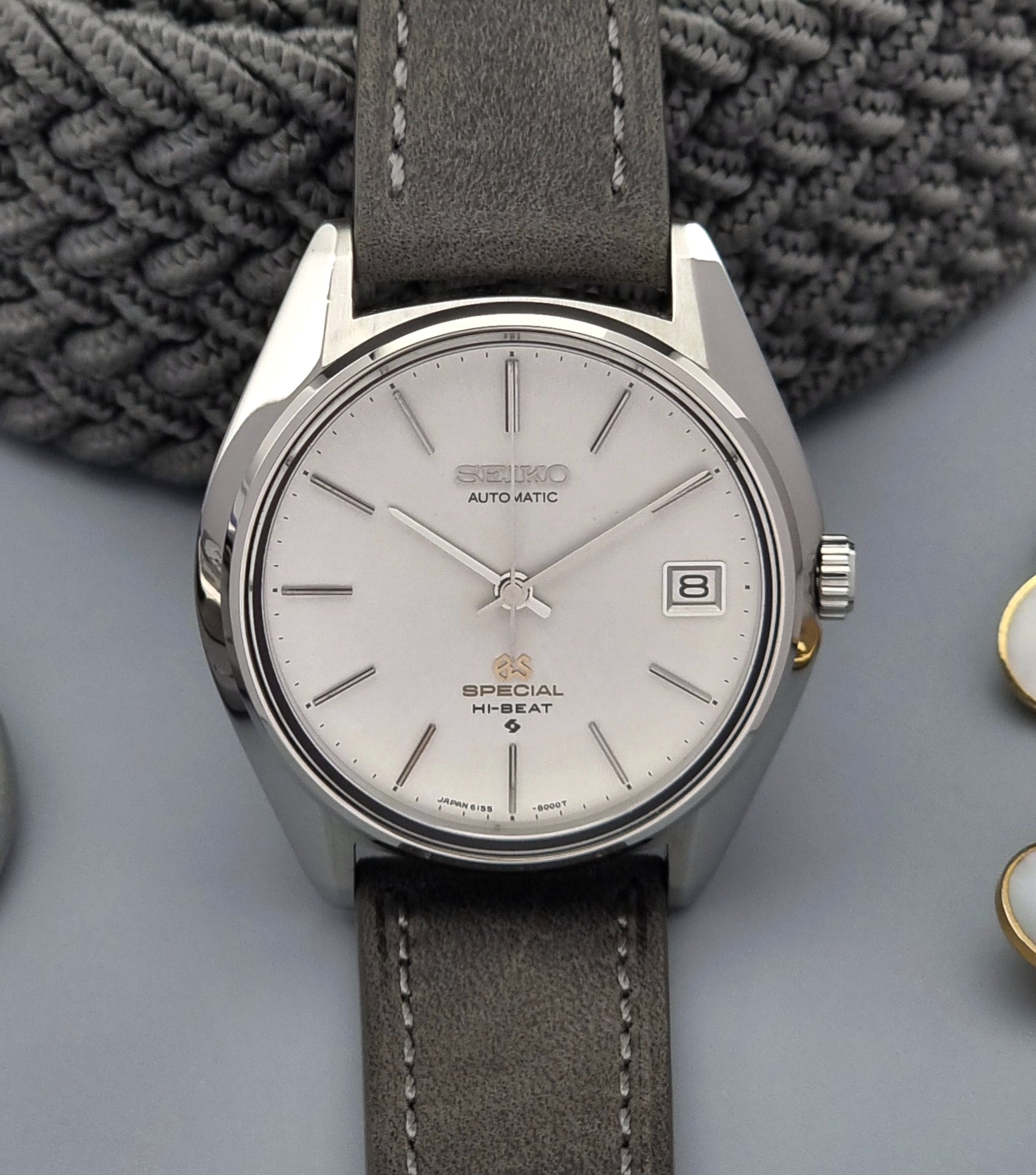 Grand Seiko wristwatch with a leather strap and silver case on a gray background