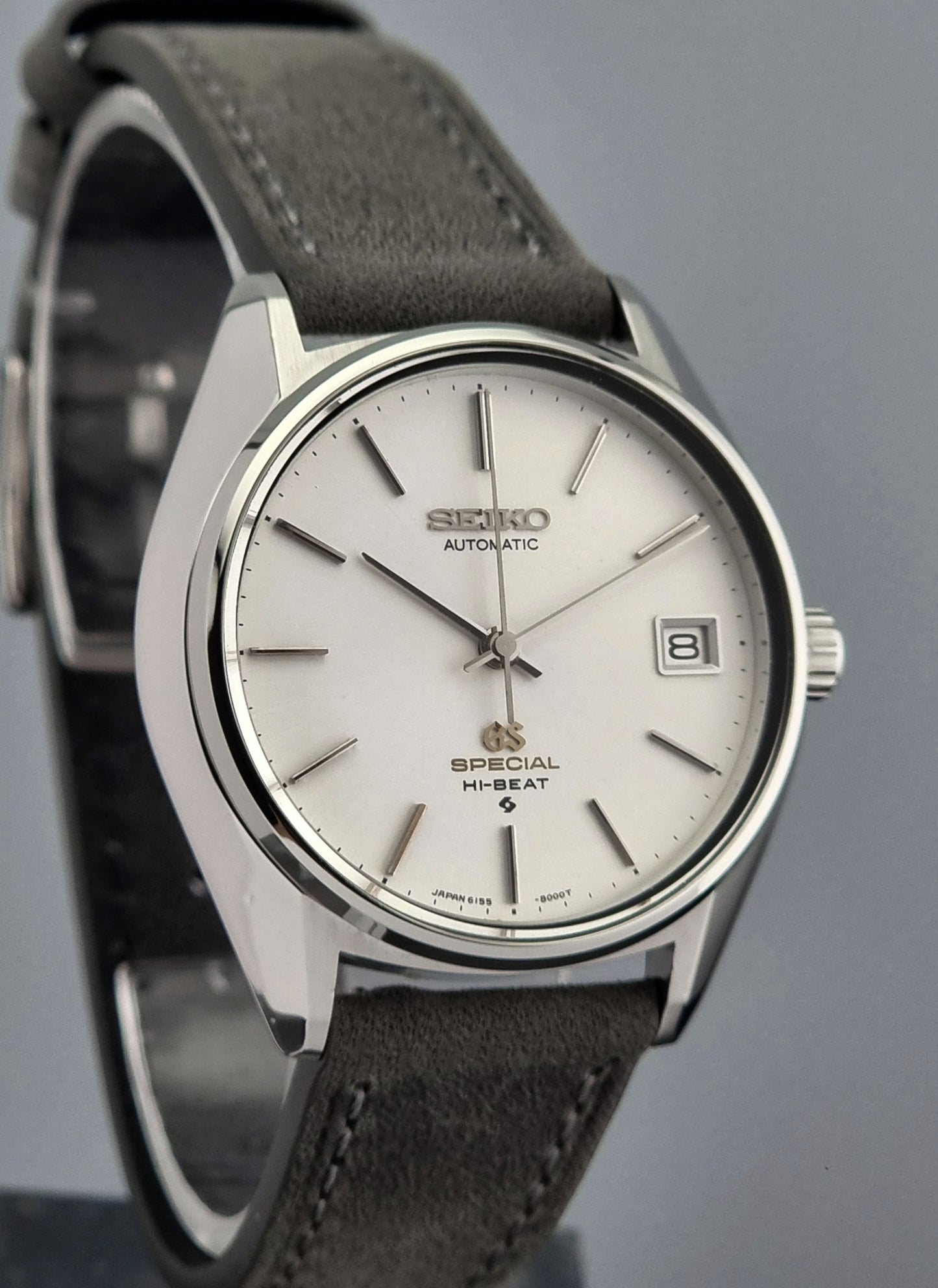 Grand Seiko wristwatch with a leather strap and silver case on a gray background