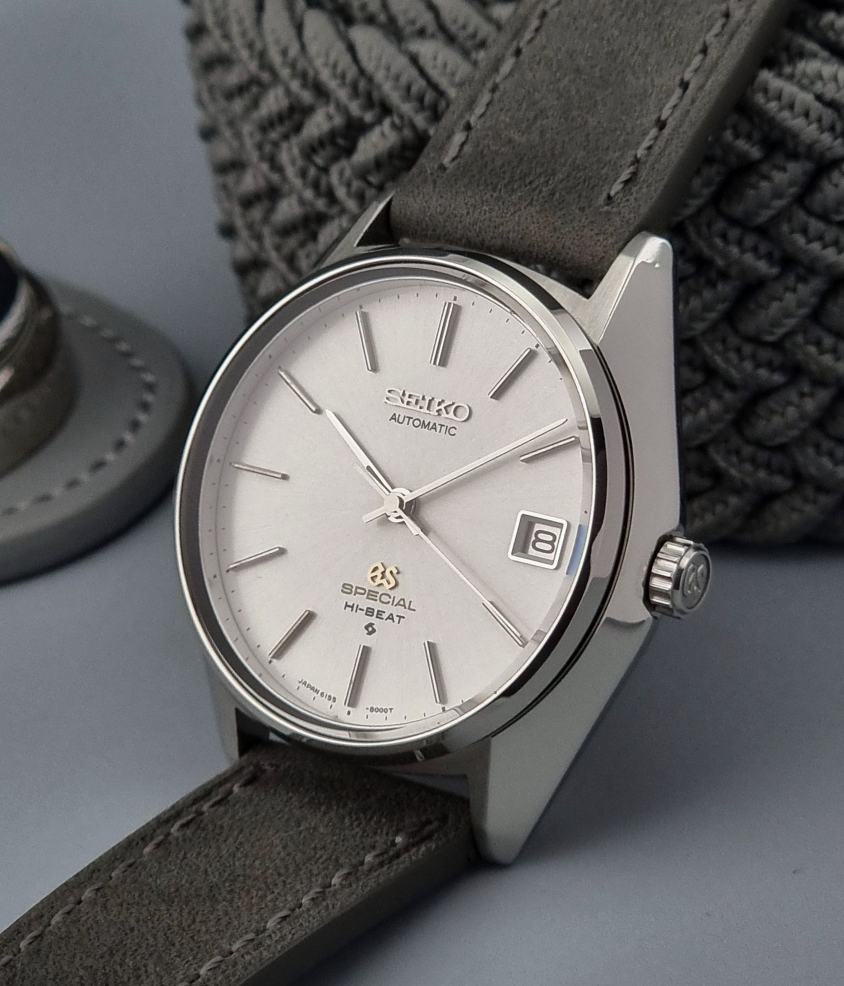 Grand Seiko wristwatch with a leather strap and silver case on a gray background