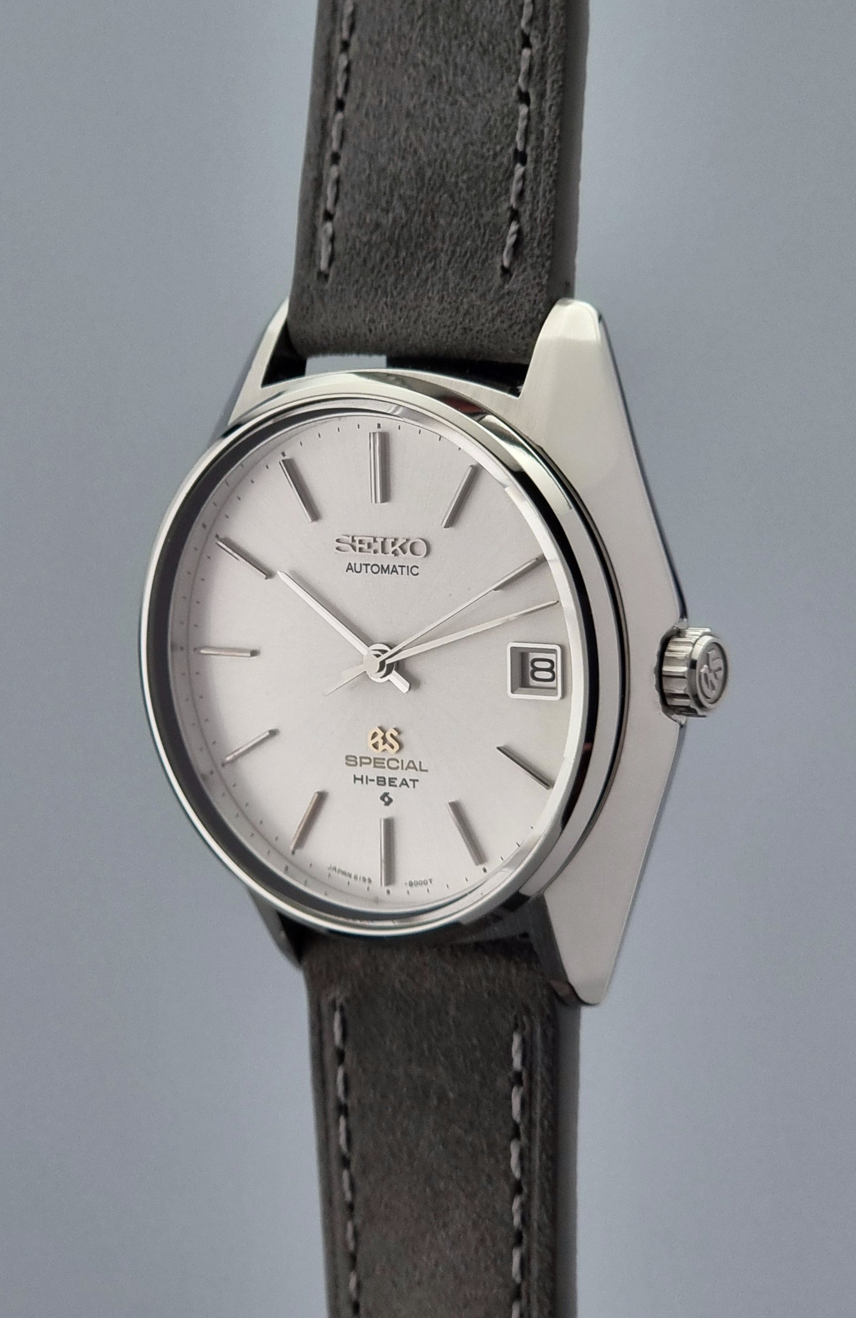 Grand Seiko wristwatch with a leather strap and silver case on a gray background