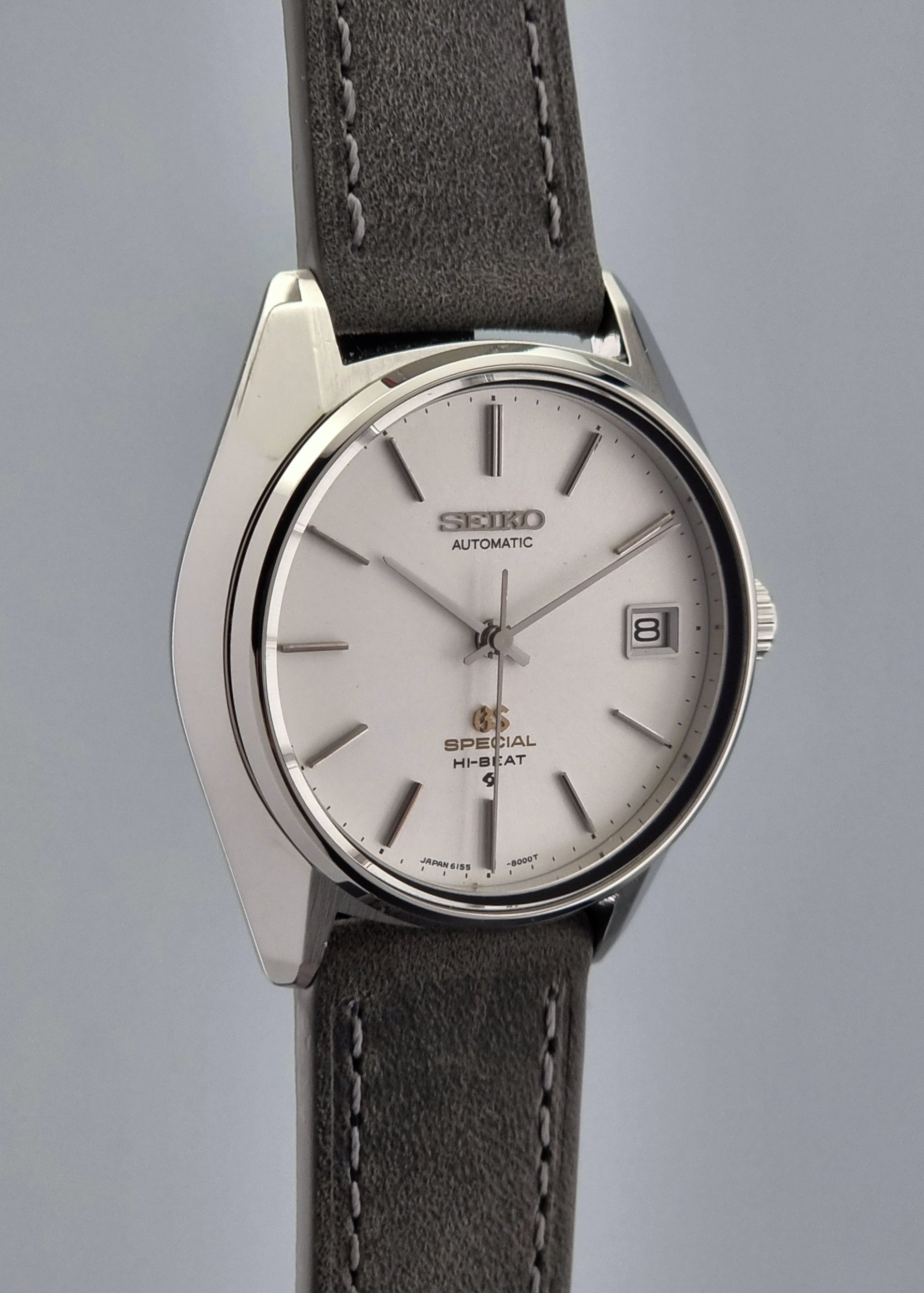 Grand Seiko wristwatch with a leather strap and silver case on a gray background