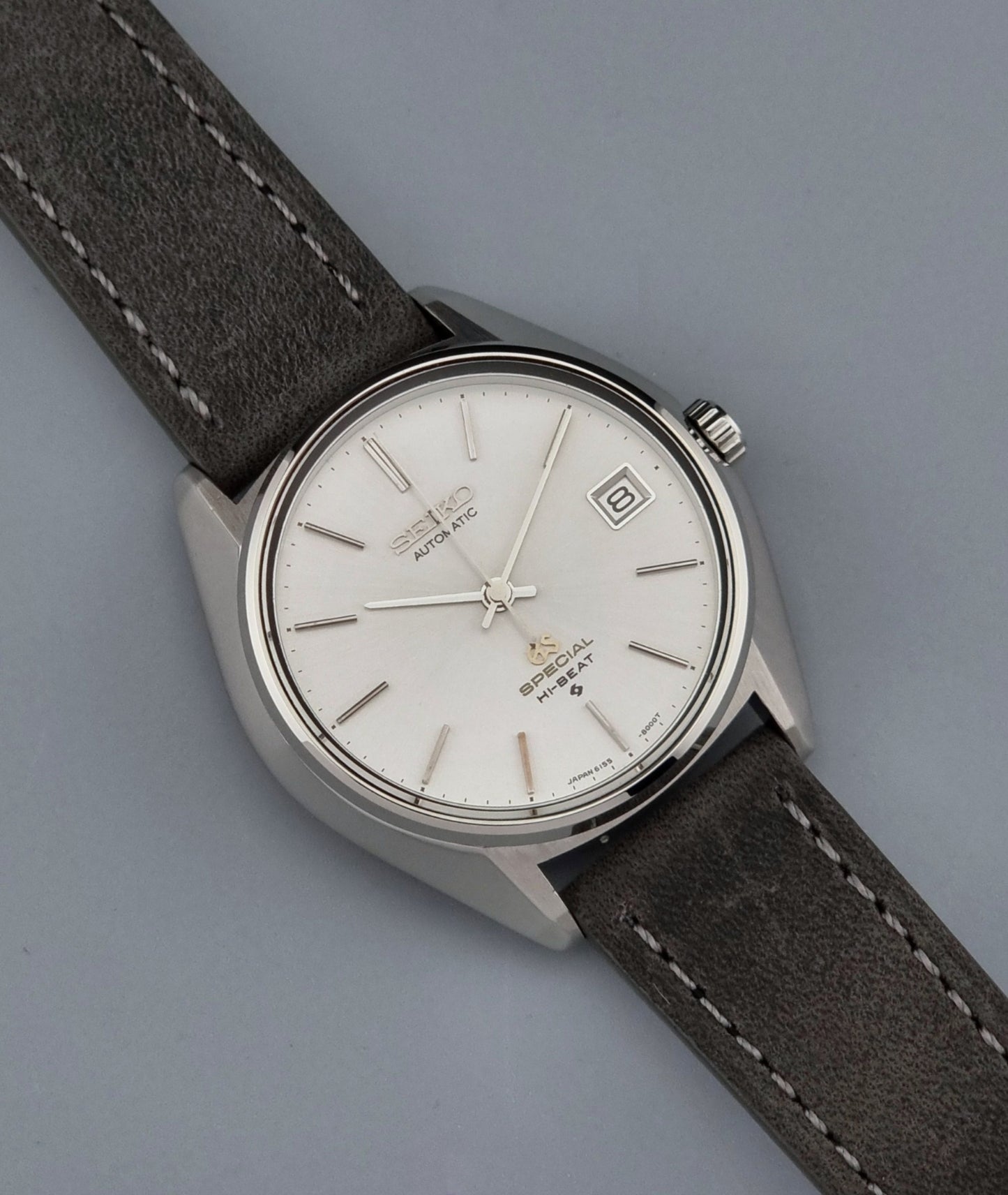 Grand Seiko wristwatch with a leather strap and silver case on a gray background