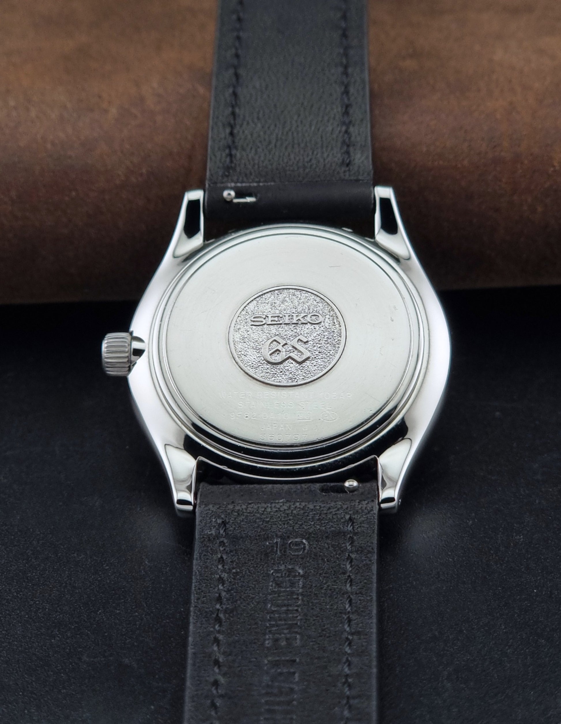 Grand Seiko SBGV001 quartz watch 9F82-0A10 with a silver-toned case,  and black leather strap, on a brown background back view