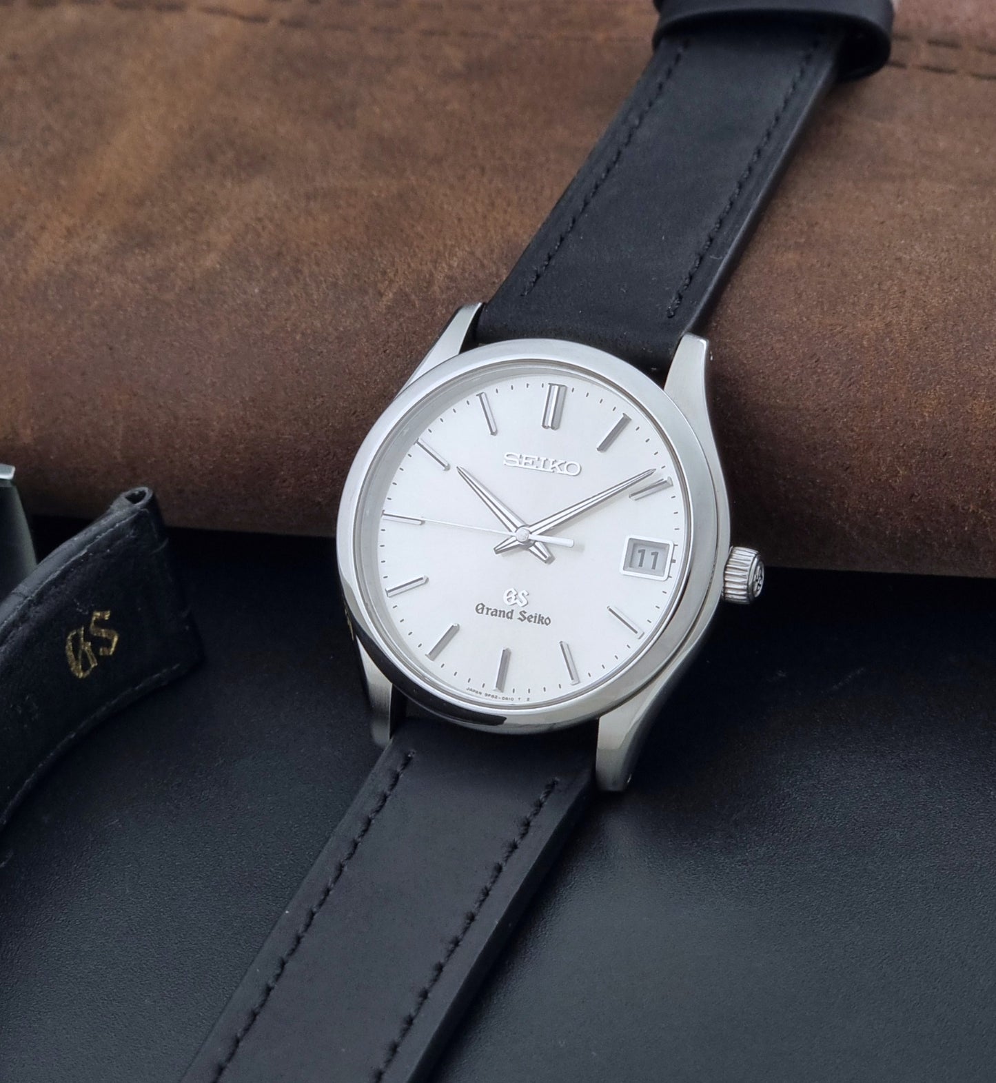 Grand Seiko SBGV001 quartz watch 9F82-0A10 with a silver-toned case,  and black leather strap, on a brown background crown view