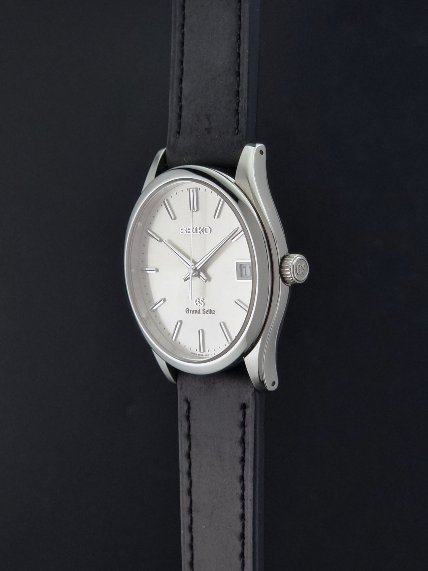 Grand Seiko SBGV001 quartz watch 9F82-0A10 with a silver-toned case,  and black leather strap, on a dark background crown profile view