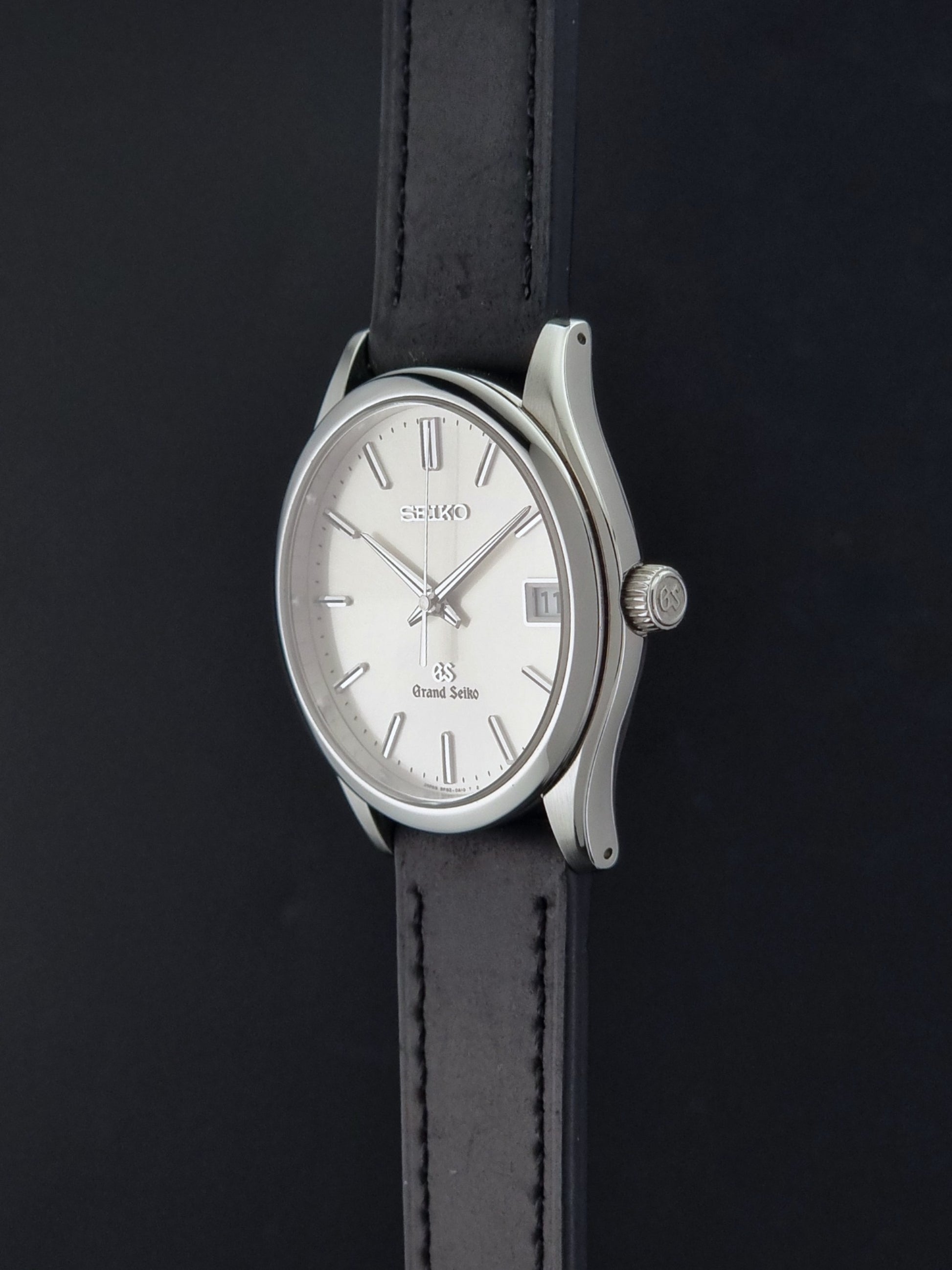 Grand Seiko SBGV001 quartz watch 9F82-0A10 with a silver-toned case,  and black leather strap, on a dark background crown profile view