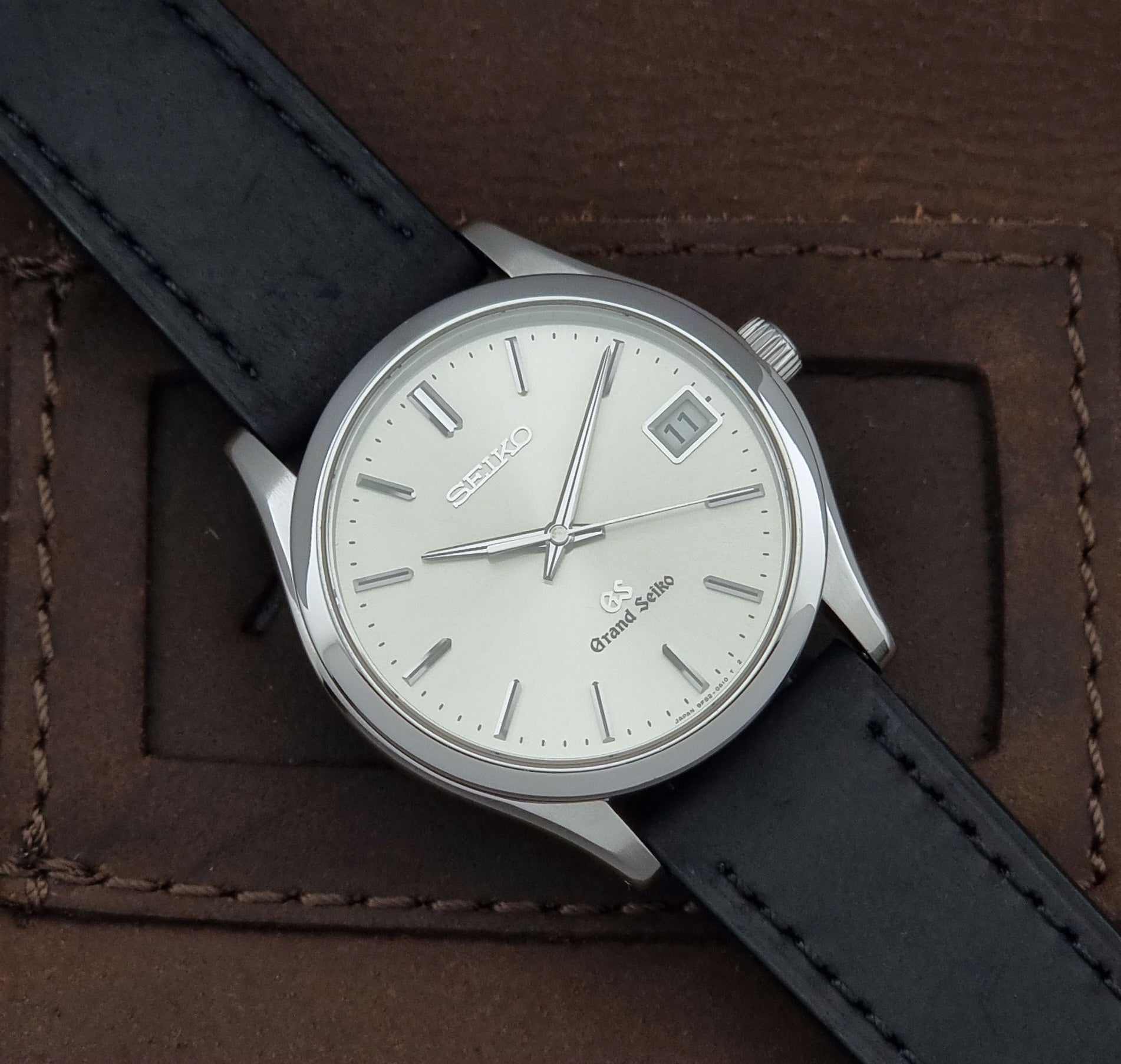 Grand Seiko SBGV001 quartz watch 9F82-0A10 with a silver-toned case,  and black leather strap, on a brown background close up dial view